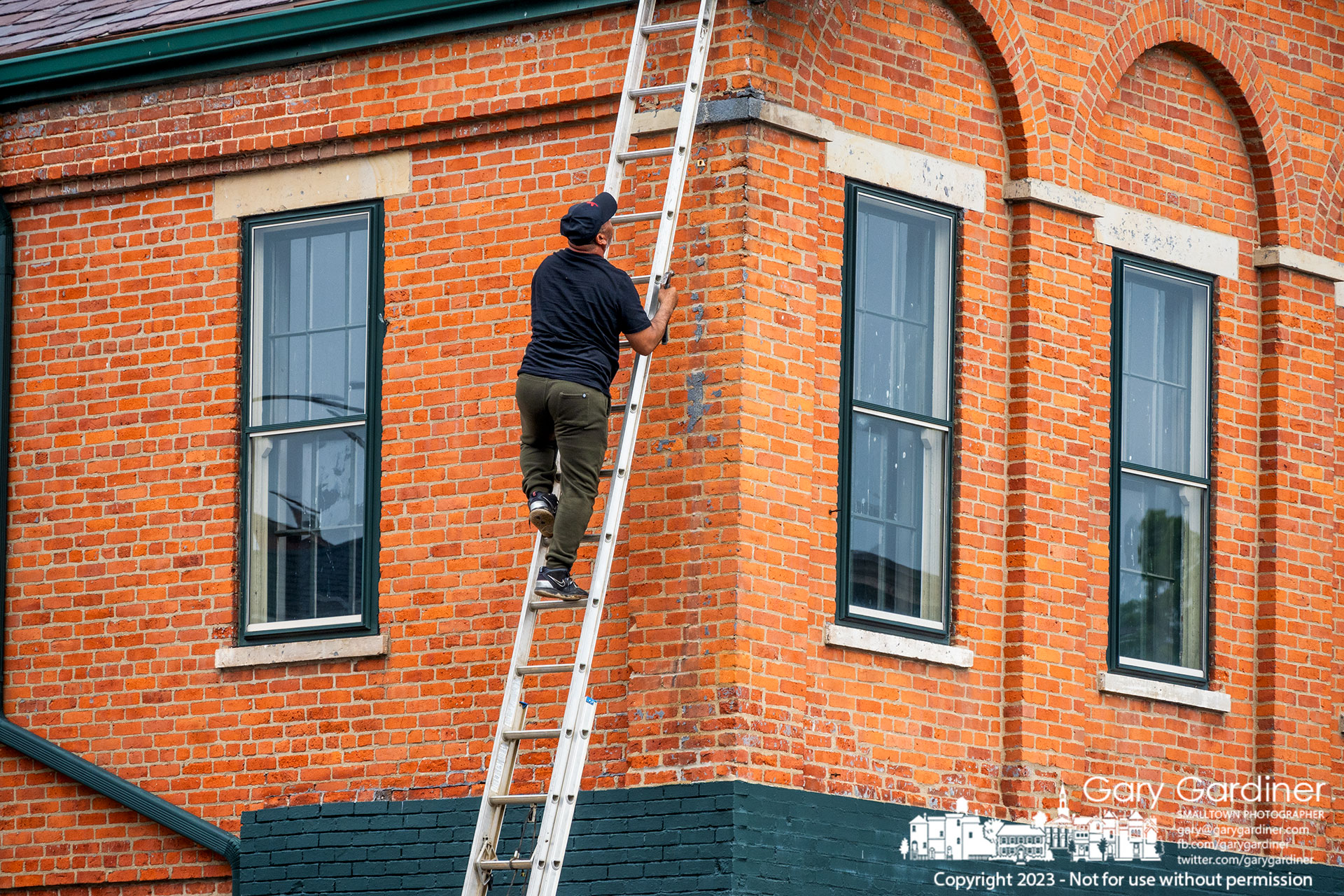 A repairman carrying a hammer checks his work after cleaning and repairing the gutter at the southeast corner of the building at State and Main with Morgan's Treasures as the first-floor business. My Final Photo for July 9, 2023.