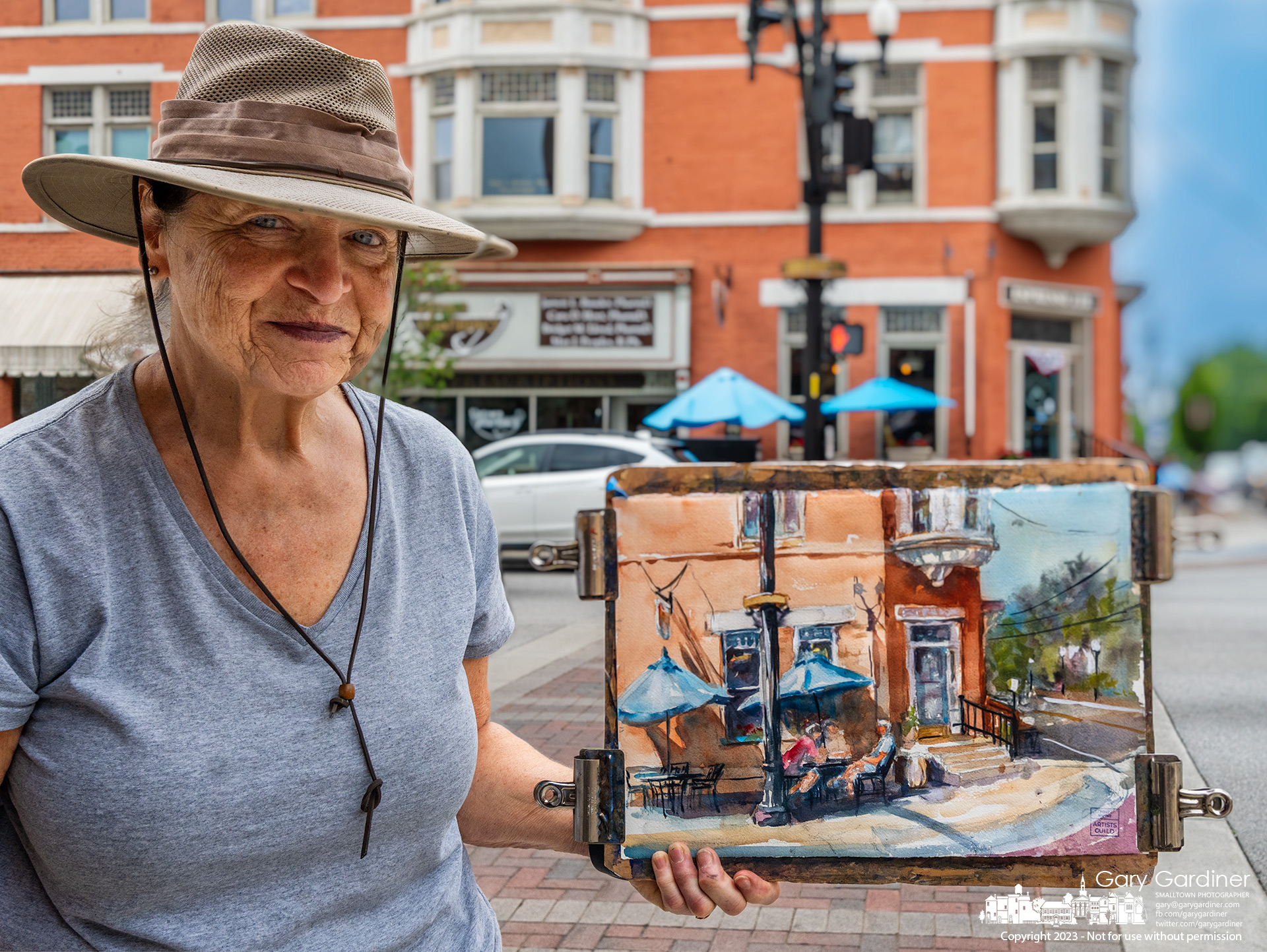 A plein air artist reluctantly holds her artwork saying it's not yet complete as she finishes a session painting at State and Main in Uptown Westerville. My Final Photo for July 18, 2023.