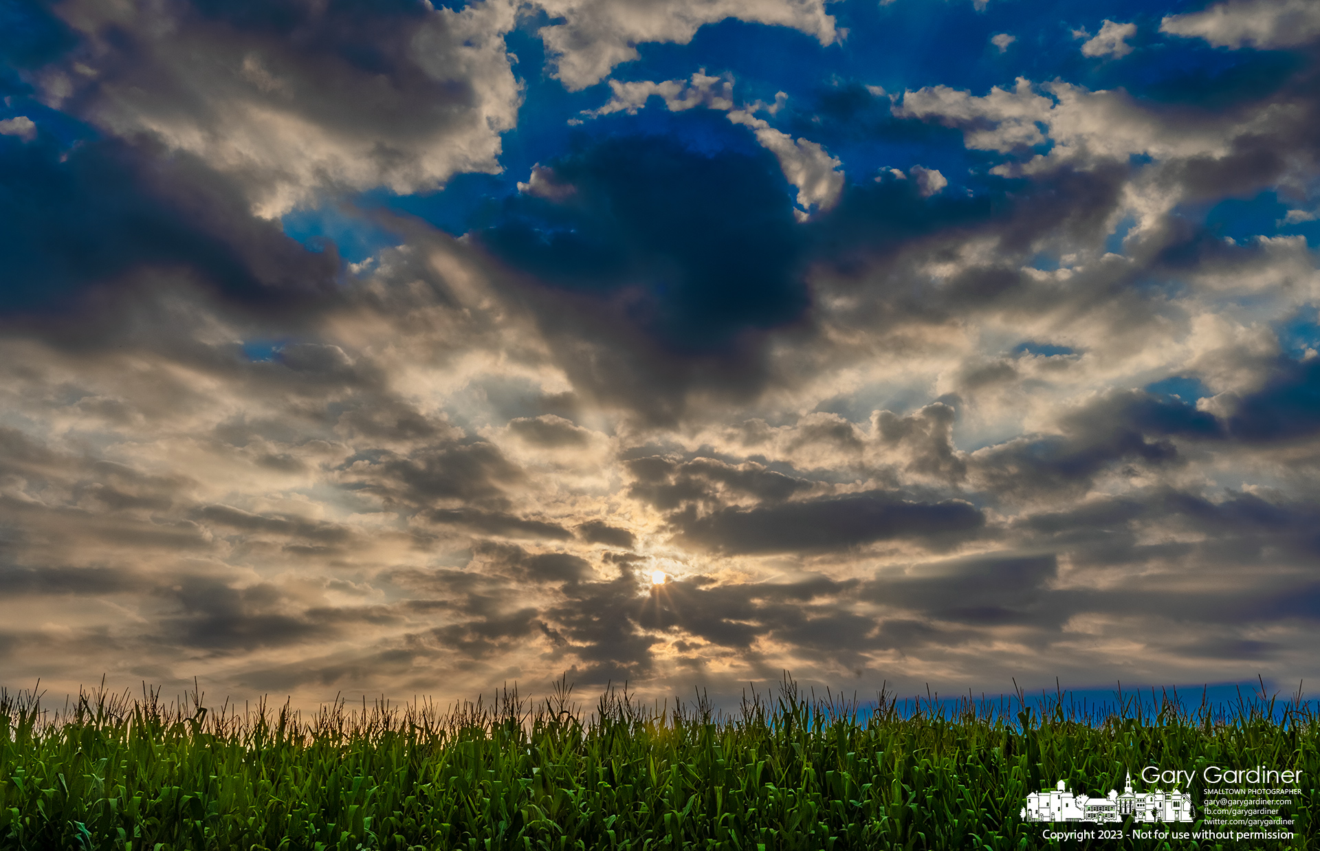 Tasseled corn grabs the rays of sun shining through clouds spreading shadows across fields and yards on a hot summer afternoon. My Final Photo for August 20, 2023.