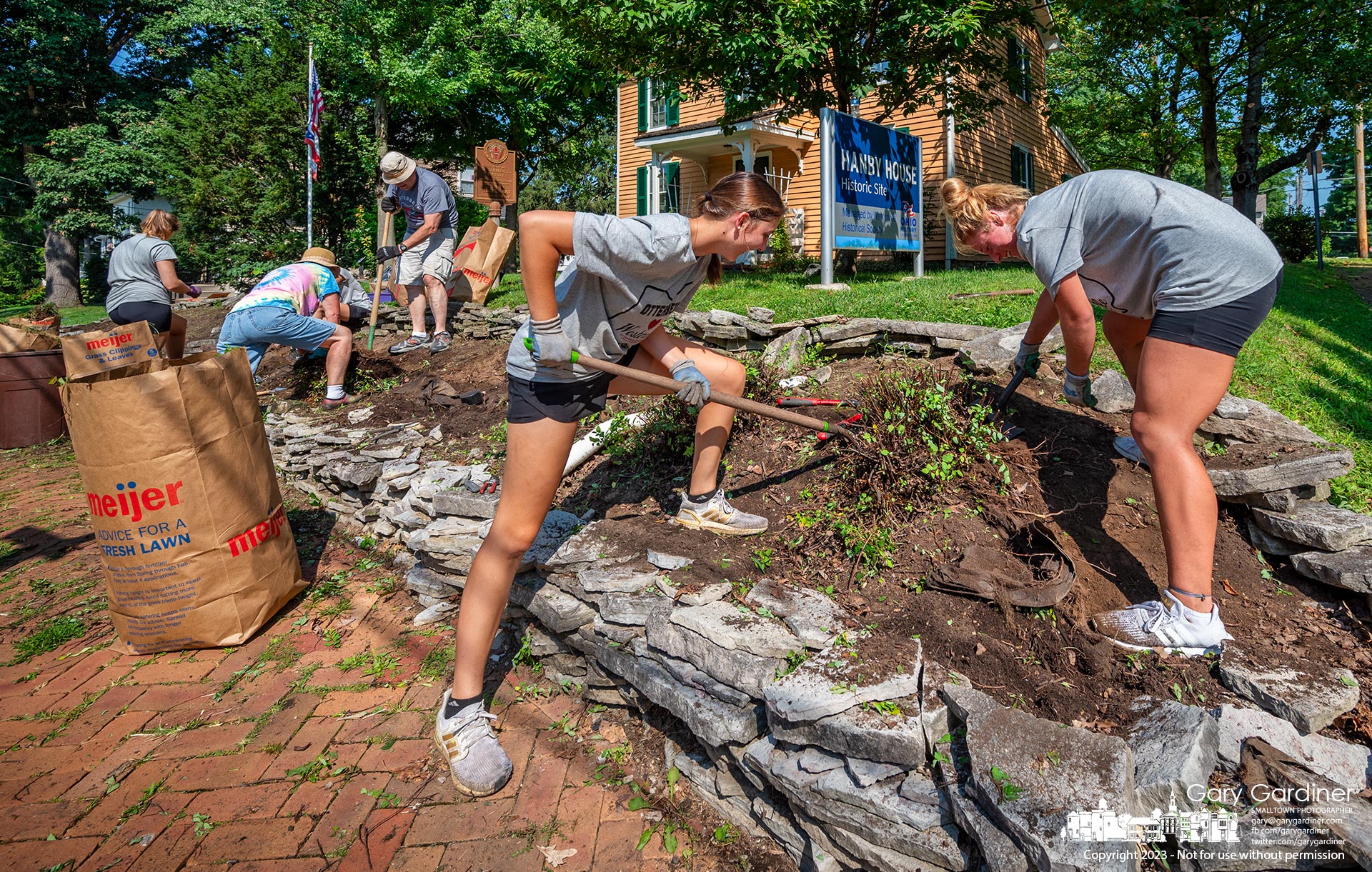 Volunteeers and Otterbein students fulfilling a community service day remove shrubs and plants from the front of the yard of the Hanby House on West Main before the historic site's lawn and rock ledge is upgraded. My Final Photo for August 19, 2023.