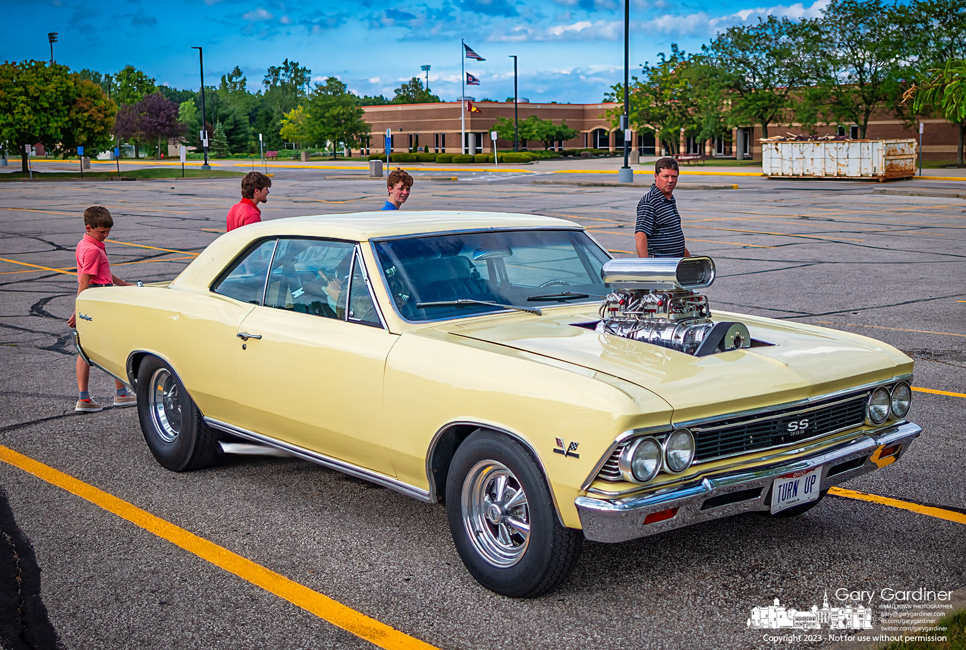 A male gathering admires a hotrod Chevy Chevelle sitting in the parking lot of Westerville North as an unofficial used car lot for passers-by to notice. My Final Photo for August 6, 2023.