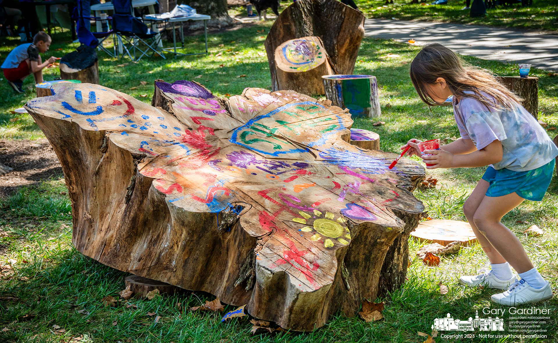 A young girl paints on the upturned stump of the American Elm tree removed this summer from Alum Creek Park North where it returned for Autumn Arborfest. My Final Photo for September 23, 2023.