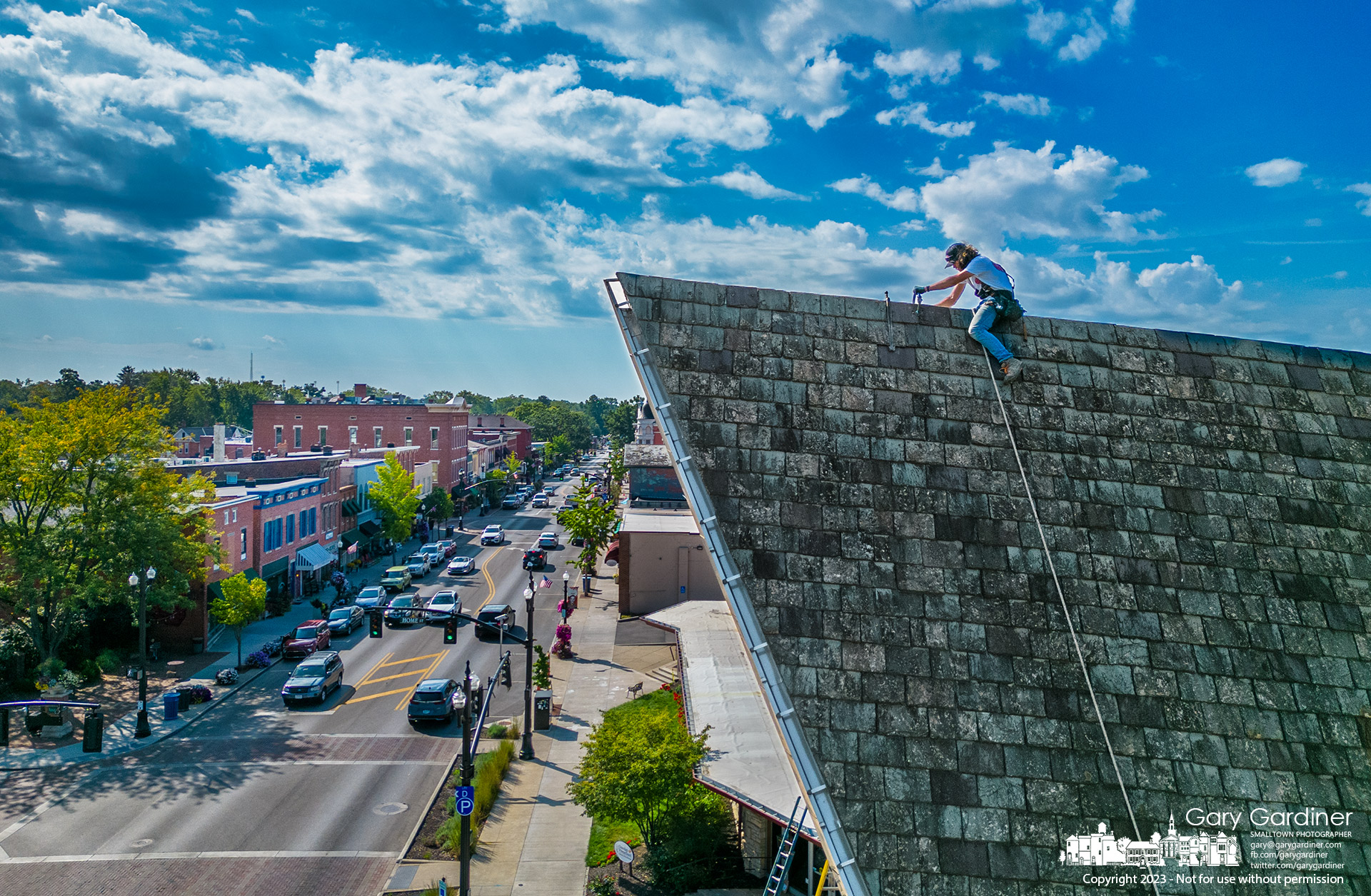 A roofer straddles the peak of the slate roof of Church of the Messiah in Uptown Westerville where he was replacing broken tiles as part of repairs to the church's roof. My Final Photo for September 6, 2023.