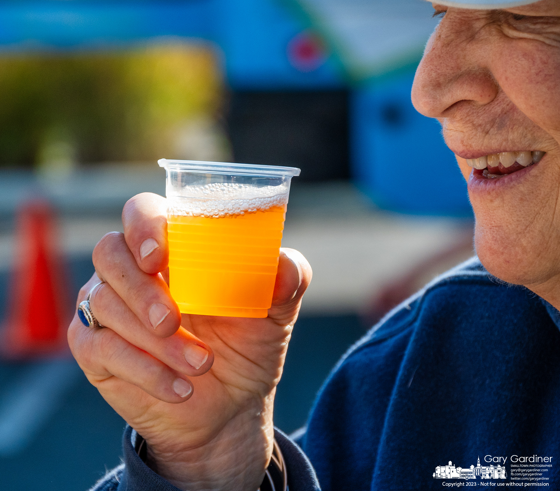 A man smiles after toasting a friend with a sample cup of apple cider from an Amish farm at the last Saturday Farmers Market of the season in Westerville. My Final Photo for September 30, 2023.