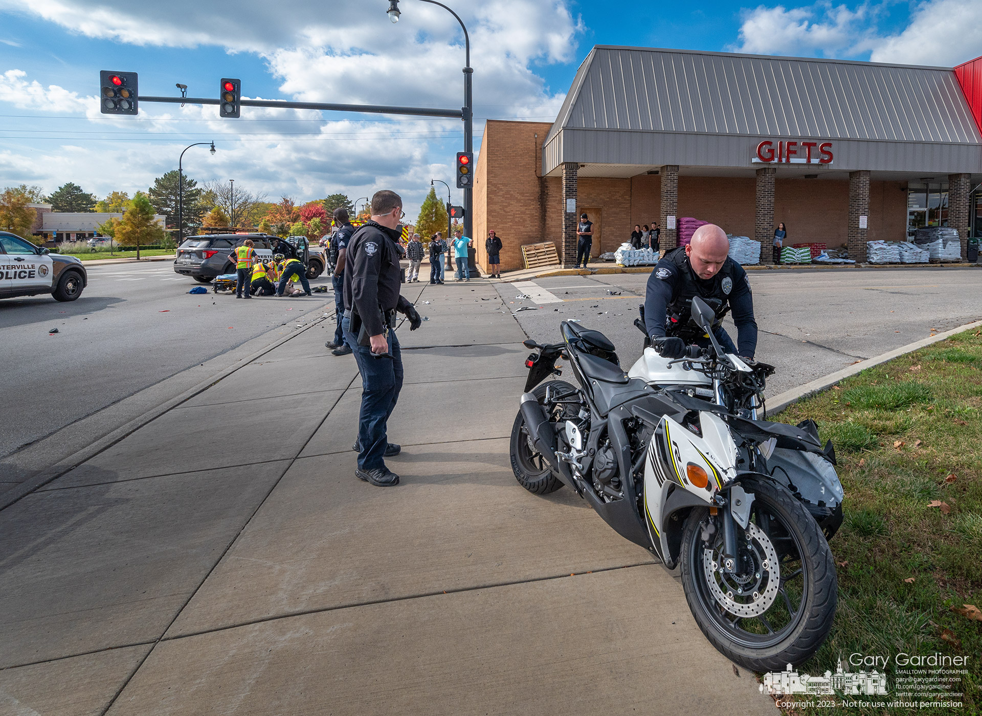 A Westerville police officer removes a motorcycle from Schrock Road where fire department paramedics treat the bike's rider after he struck the side of a truck turning in front of him. My Final Photo for October 18, 2023.