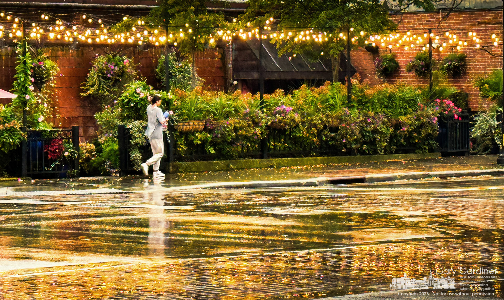 A woman walks along rain-slicked sidewalk with lights from the patio at Jimmy V's reflected in the street. My Final Photo for October 5, 2023.