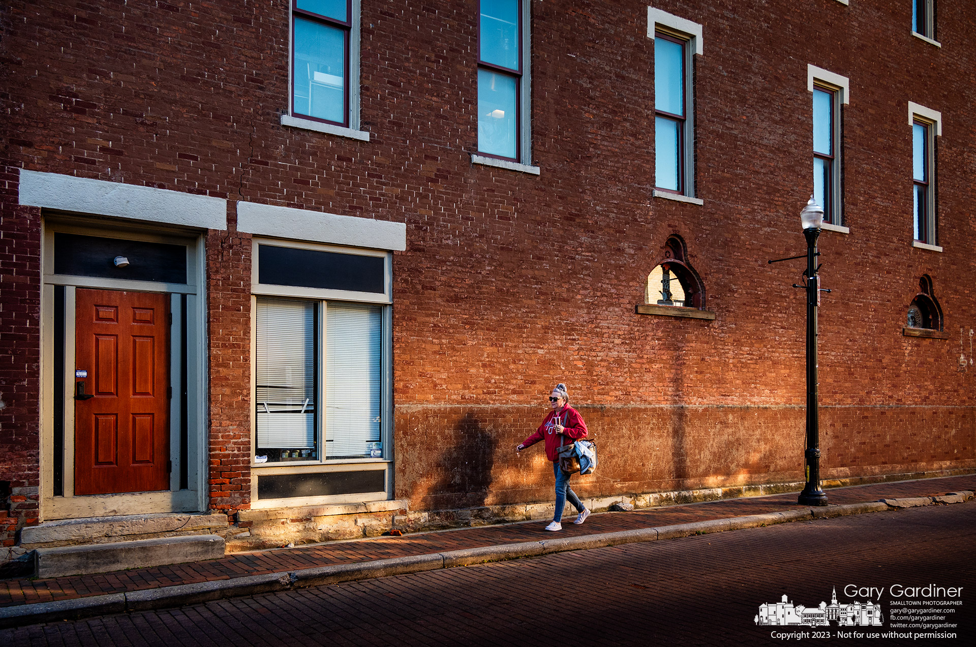 Leah Paugh walks along the wall of Old Bag of Nails where the setting sun reflected from the building across the street lights her way home. My Final Photo for November 18, 2023.