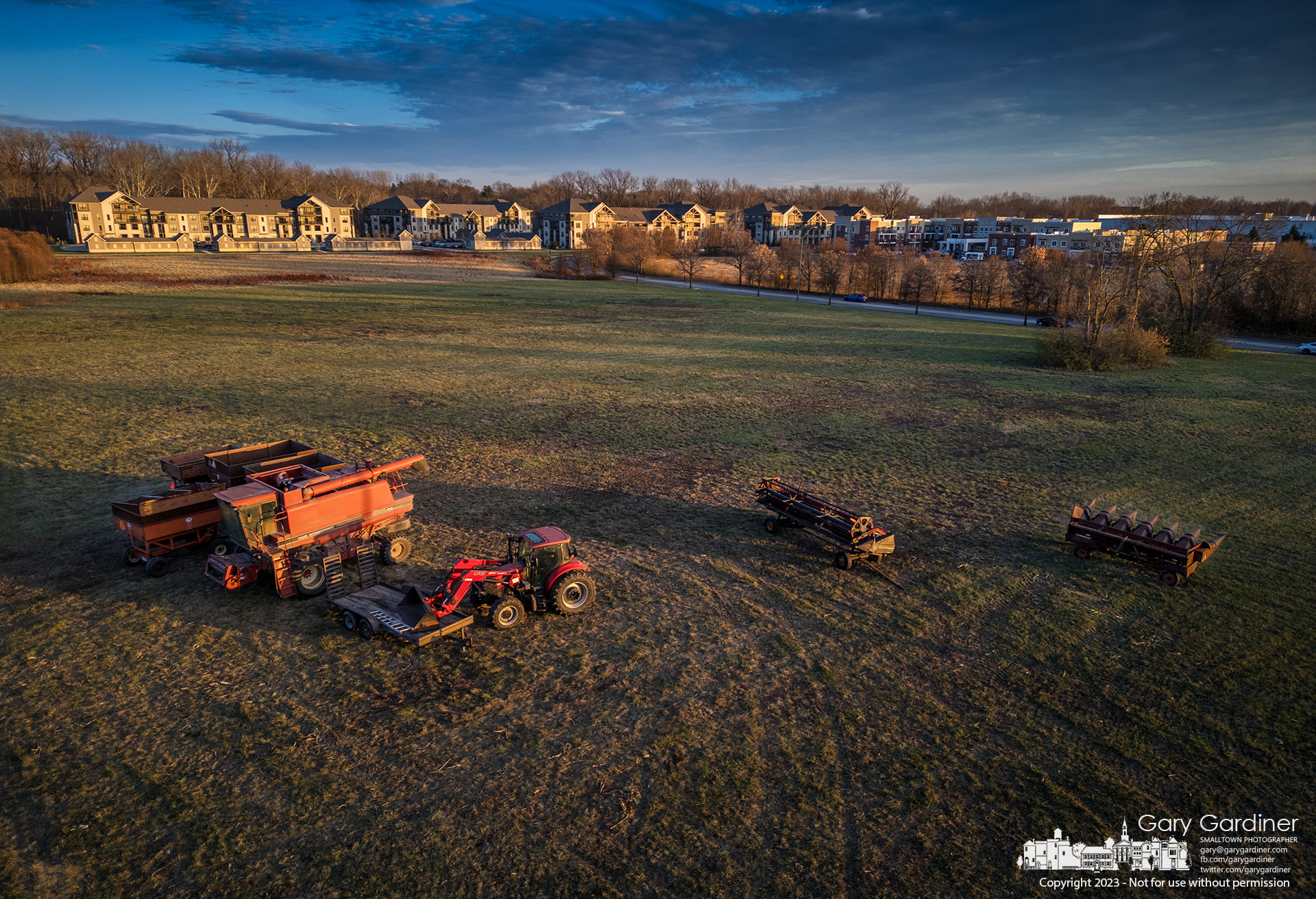 Equipment used to harvest hay, corn, and soybeans on a suburban plot of farm land sits idle at the end of the season in the hay field with an apartment building now occupying what once was farmland. My Final Photo for November 30, 2023.