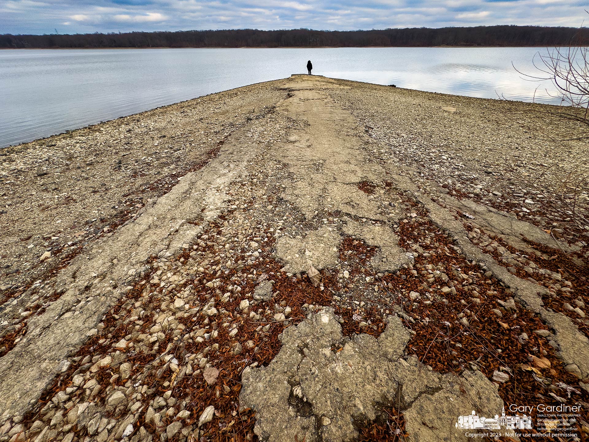 A woman stands at water's edge on the eroded remnants of Walnut Street where it enters Hoover Reservoir which was created by Hoover Dam that flooded the road and houses near the dam. My Final Photo for December 4, 2023.