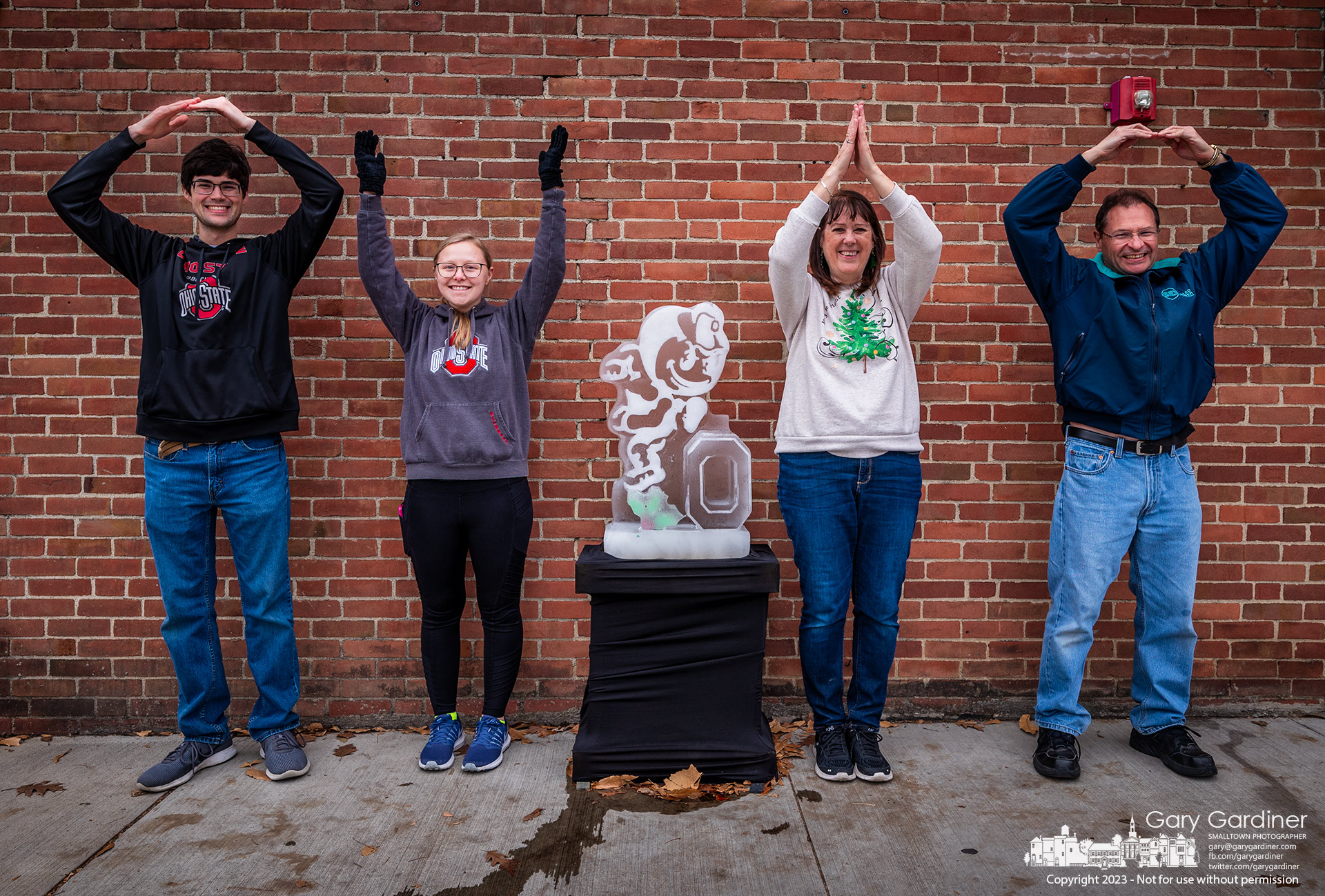 A family makes an extra effort to add to the Christmas cheer with a little Buckeye spirit as they pose for an O-H-I-O photo at the Brutus Buckeye ice sculpture at Jimmy V's in Uptown Westerville. My Final Photo for December 16, 2023.