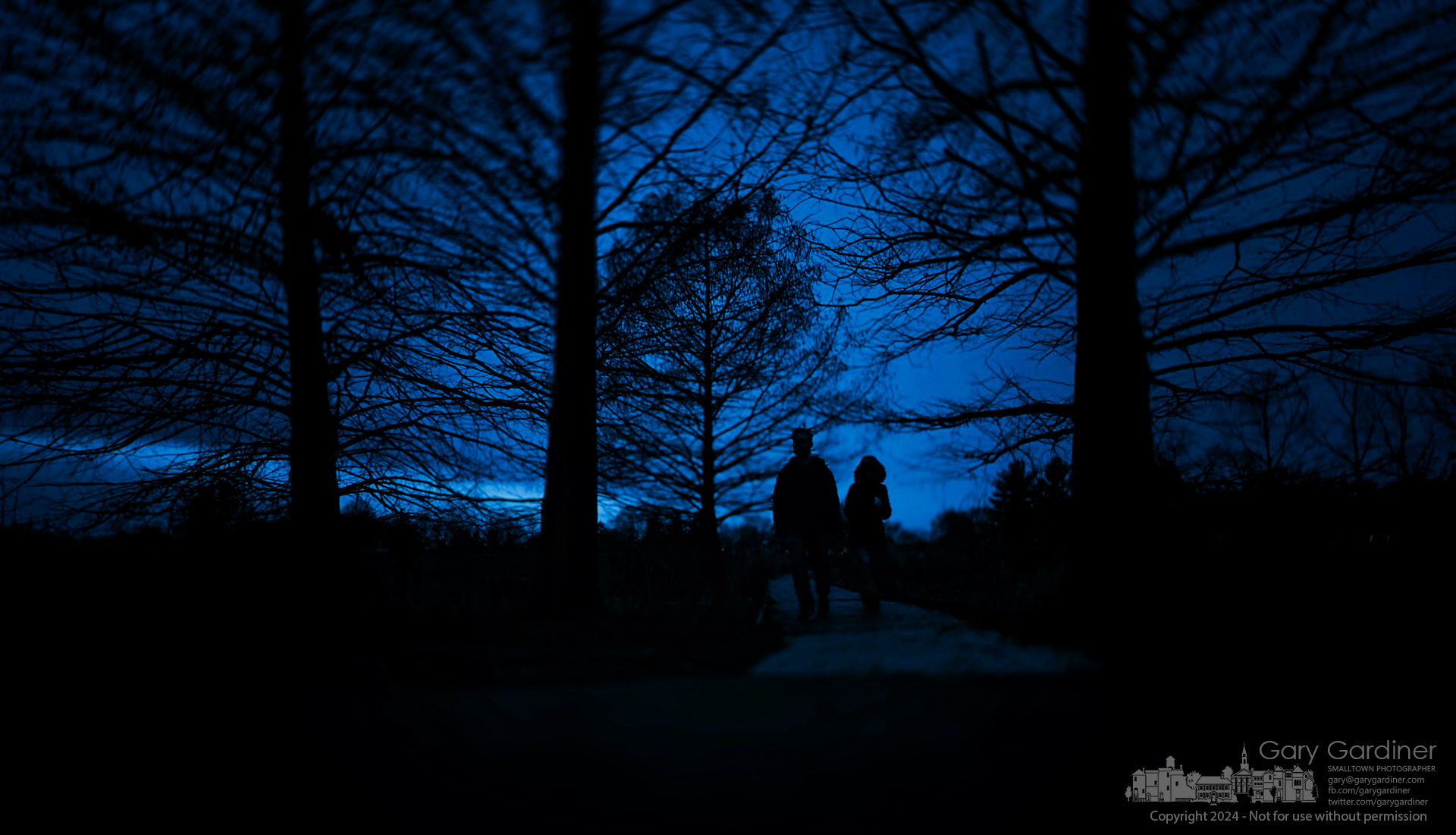 A couple walks after sunset across the footbridge spanning a portion of the wetlands at Highlands Park in Westerville. My Final Photo for January 8, 2024.