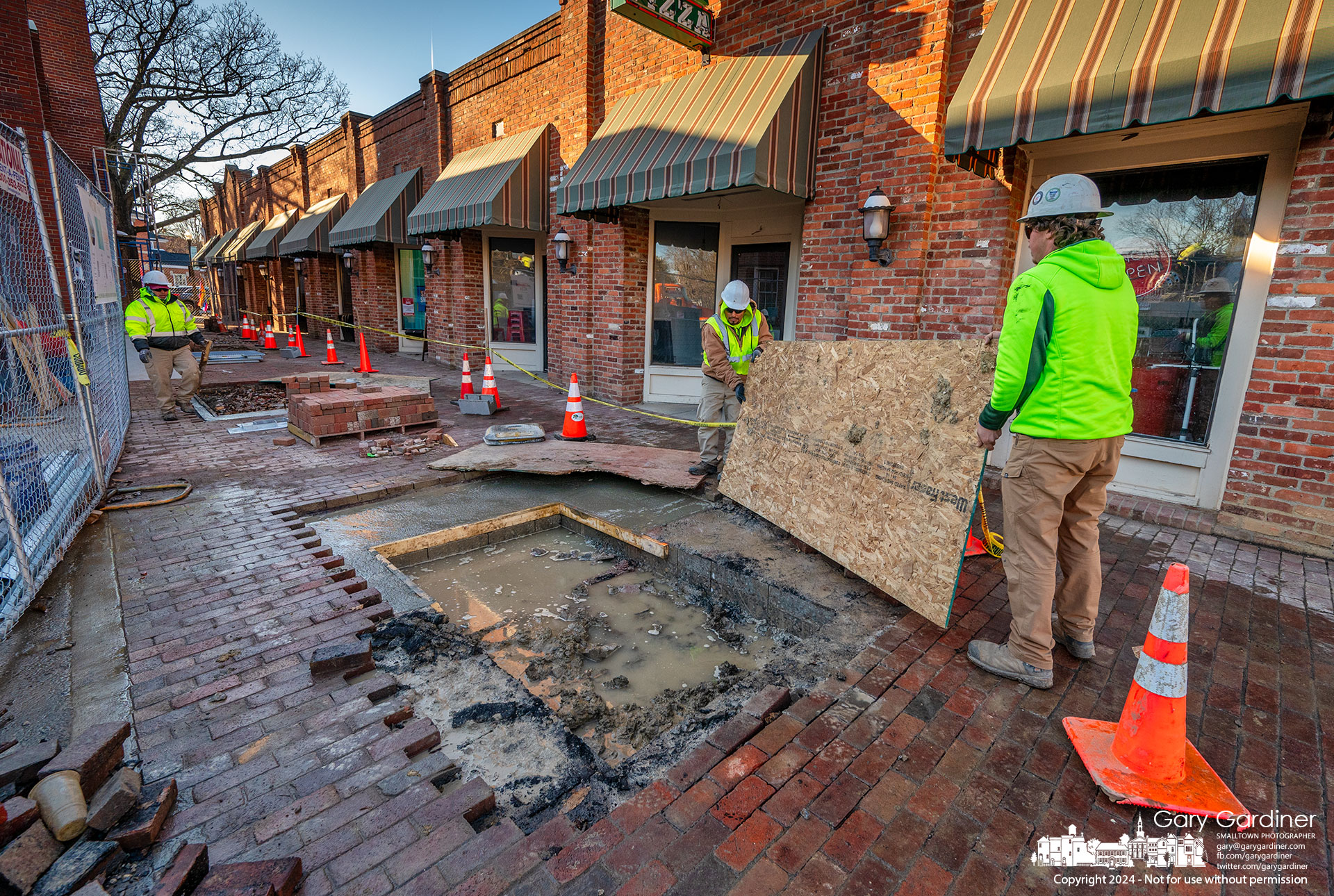 Workers cover freshly poured concrete designed to be platforms for grating surrounding trees to be planted in the Brick Walk between Java Central and High Bank Distillery. My Final Photo for February 29, 2024.