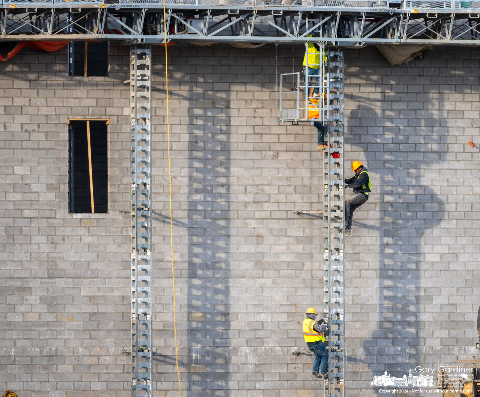 Brick masons lower themselves on the ladder and support structure from a work platform at one of the elevator shafts for an apartment complex being built at the Galaxy at Polaris on Ikea Way. My Final Photo for February 21, 2024.
