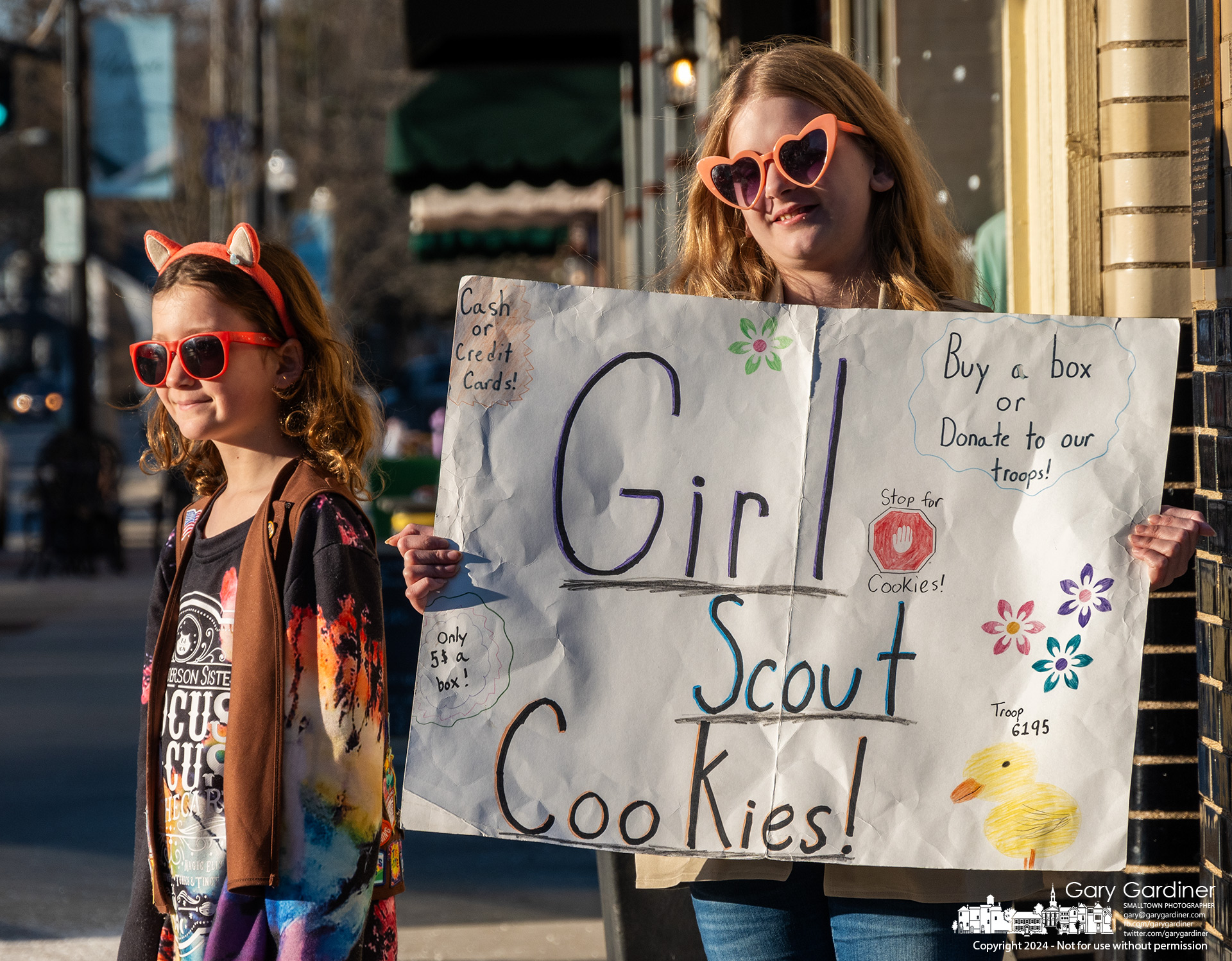 Girl Scouts from Troop 6395 wearing sunglasses to shield their eyes from the late afternoon sun offer encouragement to buyers at State and Main just a few feet from their Girl Scout Cookie stand where they accept cash, credit cards, and Venmo. My Final Photo for February 20, 2024.