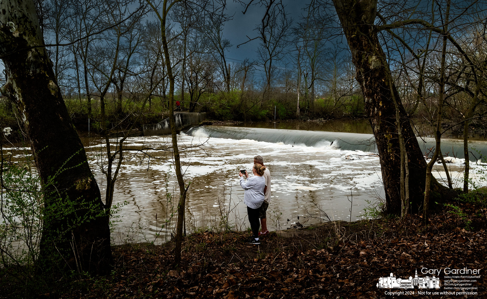 A couple watches a blue heron fish the rapid waters flowing over the Alum Creek North low-head dam after several days of rain raised the creek's level as more storms approached. My Final Photo for April 2, 2024.
