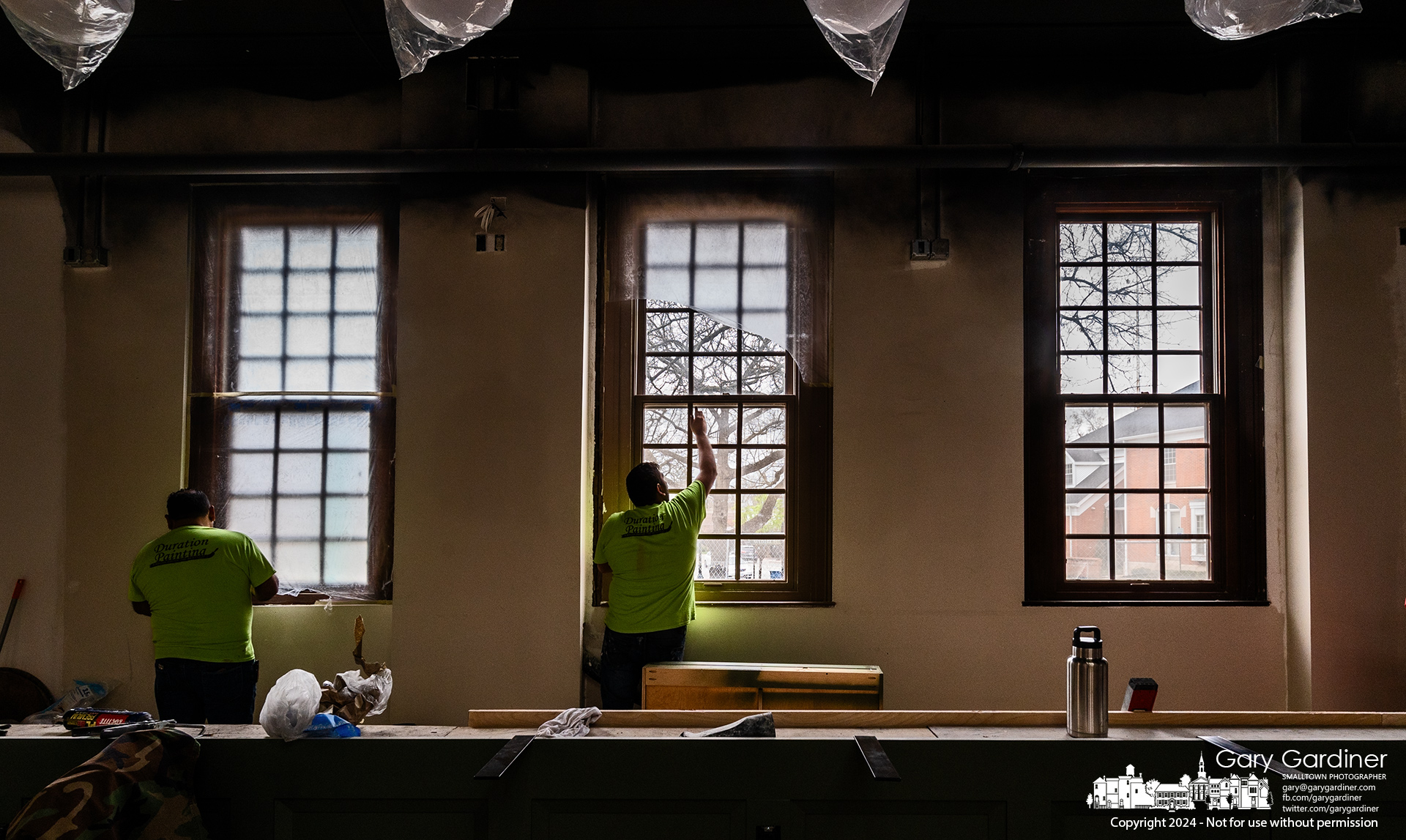 Workers remove plastic sheets taped to windows inside the High Bank Distillery restaurant to keep the windows from overspray during painting. My Final Photo for April 9, 2024.