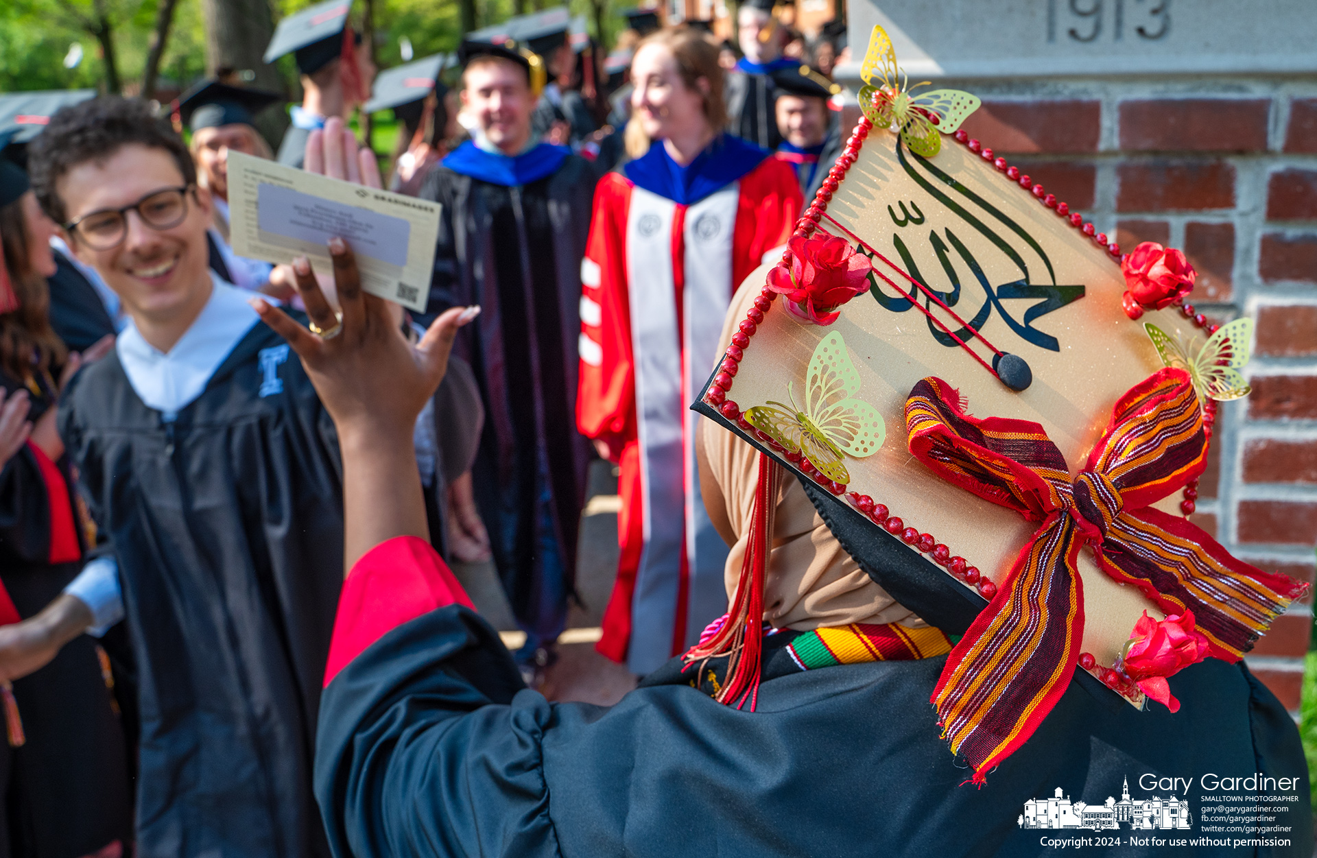 An Otterbein graduate wearing a mortar board emblazoned with "My Dream" in Arabic high-fives another graduate as they begin the procession for commencement ceremonies Sunday morning. My Final Photo for April 28, 2024.