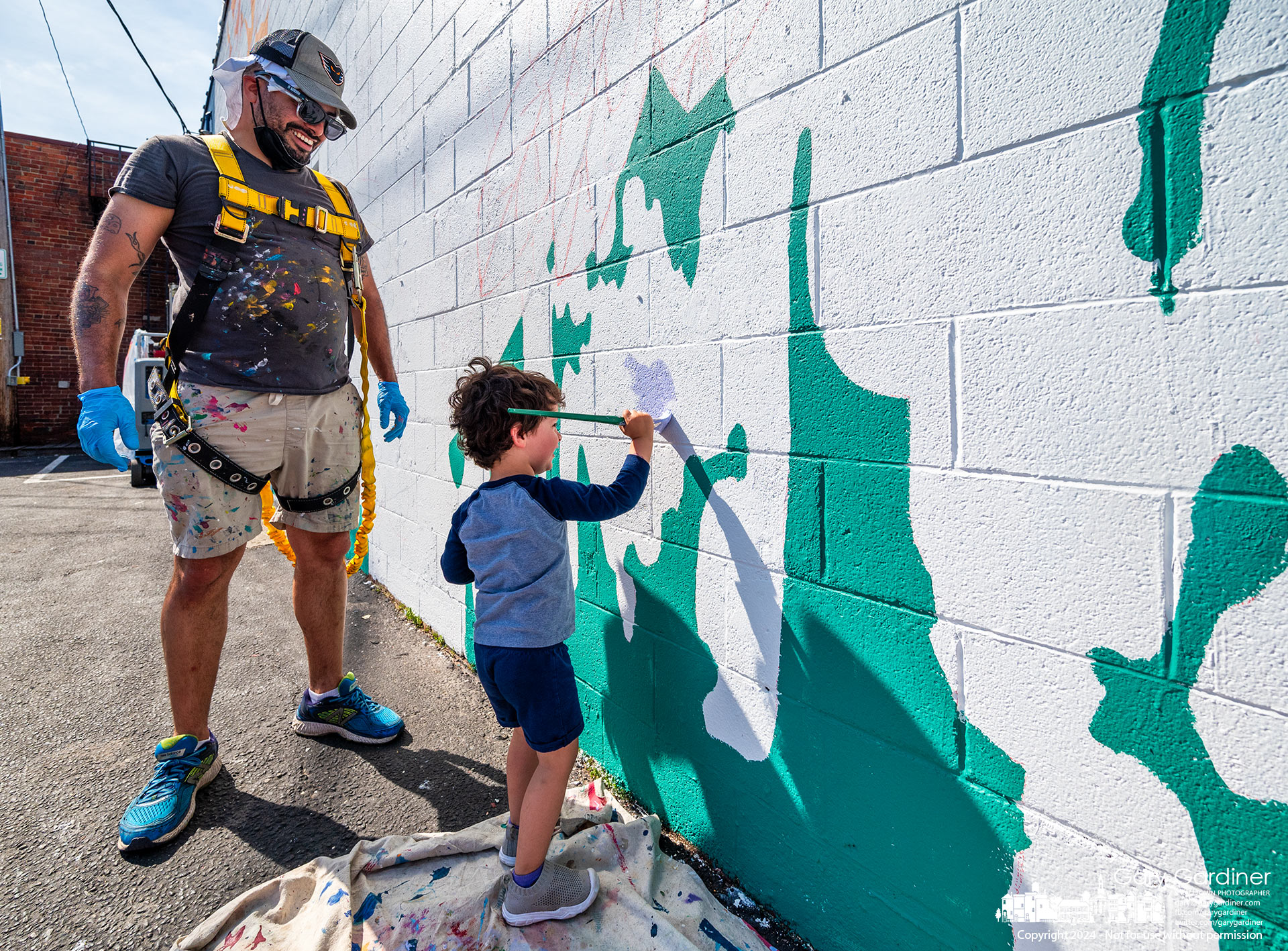 Under the tutelage of his artist father, Adam, two-year-old Ray Hernandez applies paint to a section of the "Peace" mural Hernandez is painting in Uptown Westerville. My Final Photo for April 16, 2024.