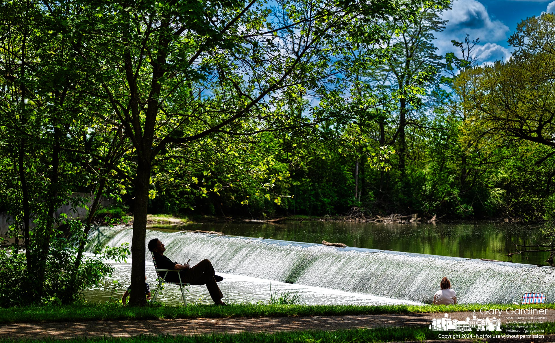 A man sits in the shade of a maple tree while his family fishes the waters of Alum Creek just below the dam at Alum Creek Park North in Westerville. My Final Photo for May 5, 2024.