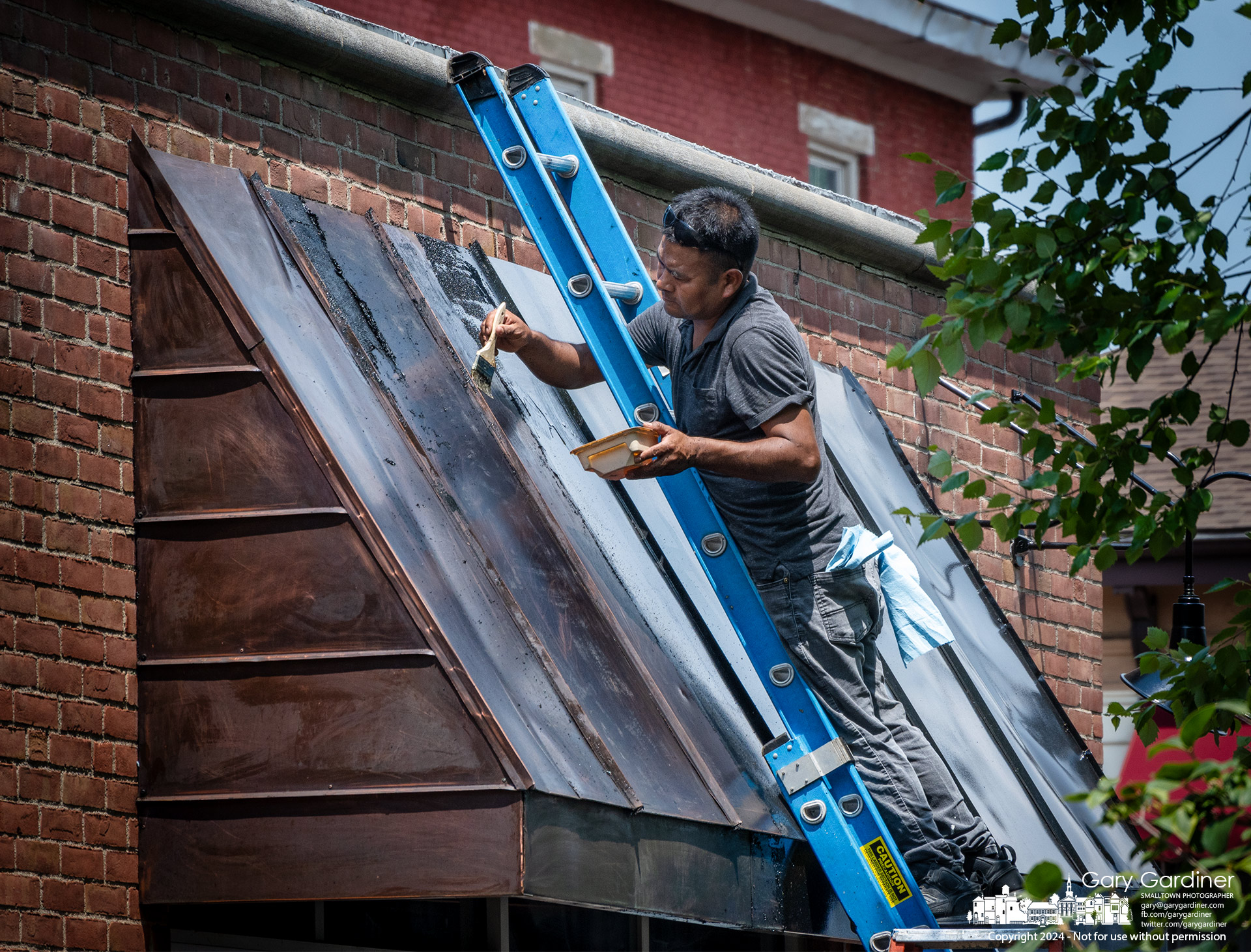 A worker applies paint stripper to the copper awnings at Jimmy V's to remove black paint applied without approval from the city Uptown Review Board. My Final Photo for June 17, 2024.