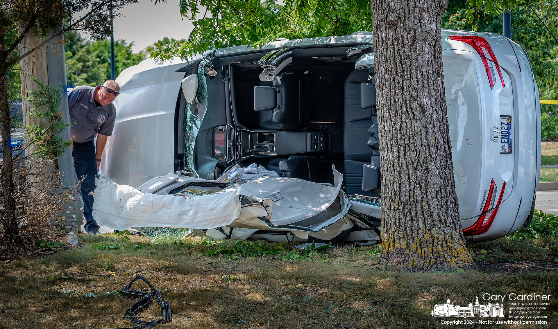 A Westerville Police crash investigator inspects the scene of a car crash Friday on Sugar Grove Square where a driver went left of center and struck a utility pole guide wire flipping it on its side and into two trees. My Final Photo for July 26, 2024.