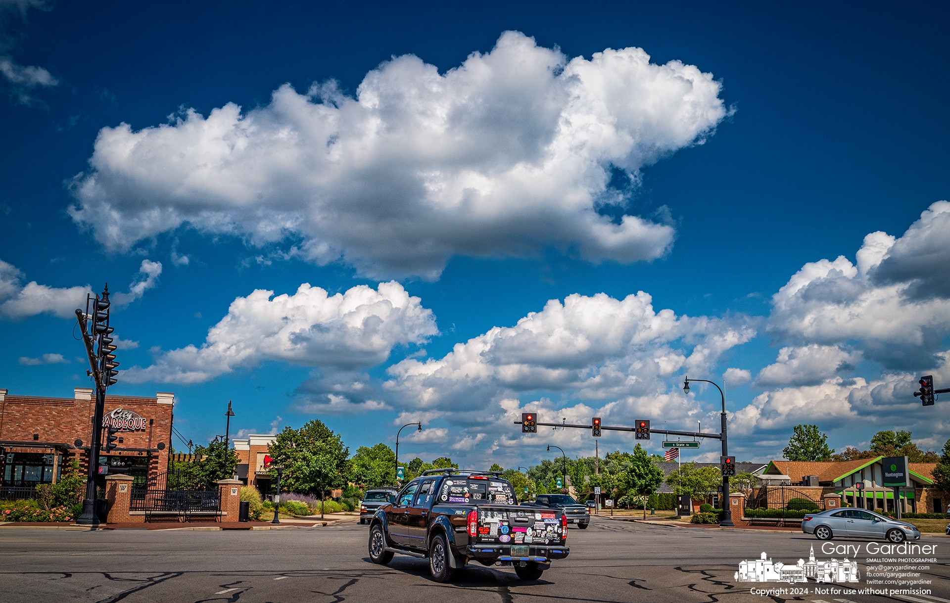 A pickup truck plastered with a melange of stickers turns onto State Street under a cumulus cloud-filled sky. My Final Photo for July 30, 2024.