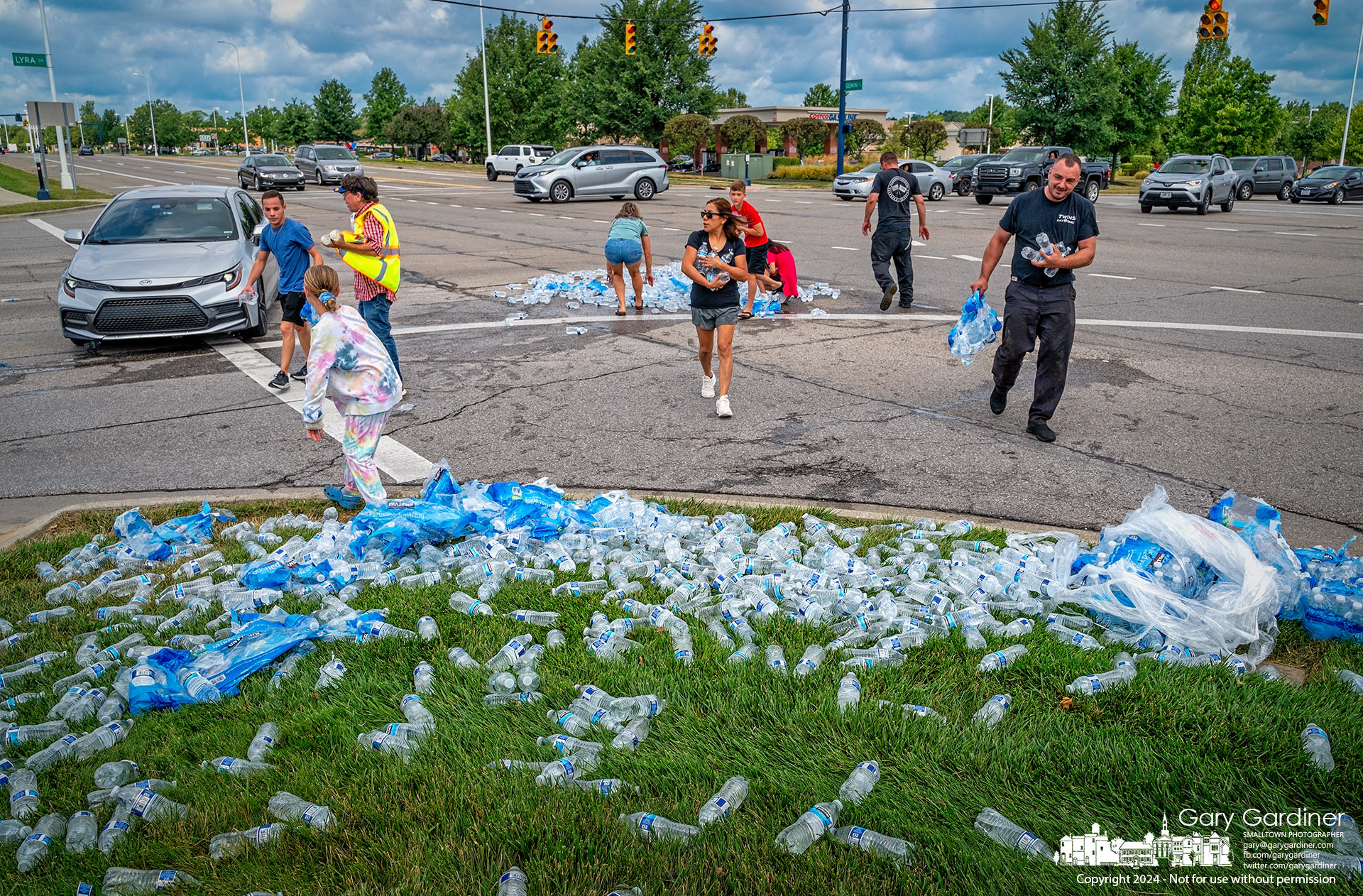 Good Samaritans help a flatbed truck driver retrieve the load of water bottles that fell from his truck when he turned onto Gemini Parkway, causing a minor traffic jam as the roadway was cleared. My Final Photo for July 31, 2024.