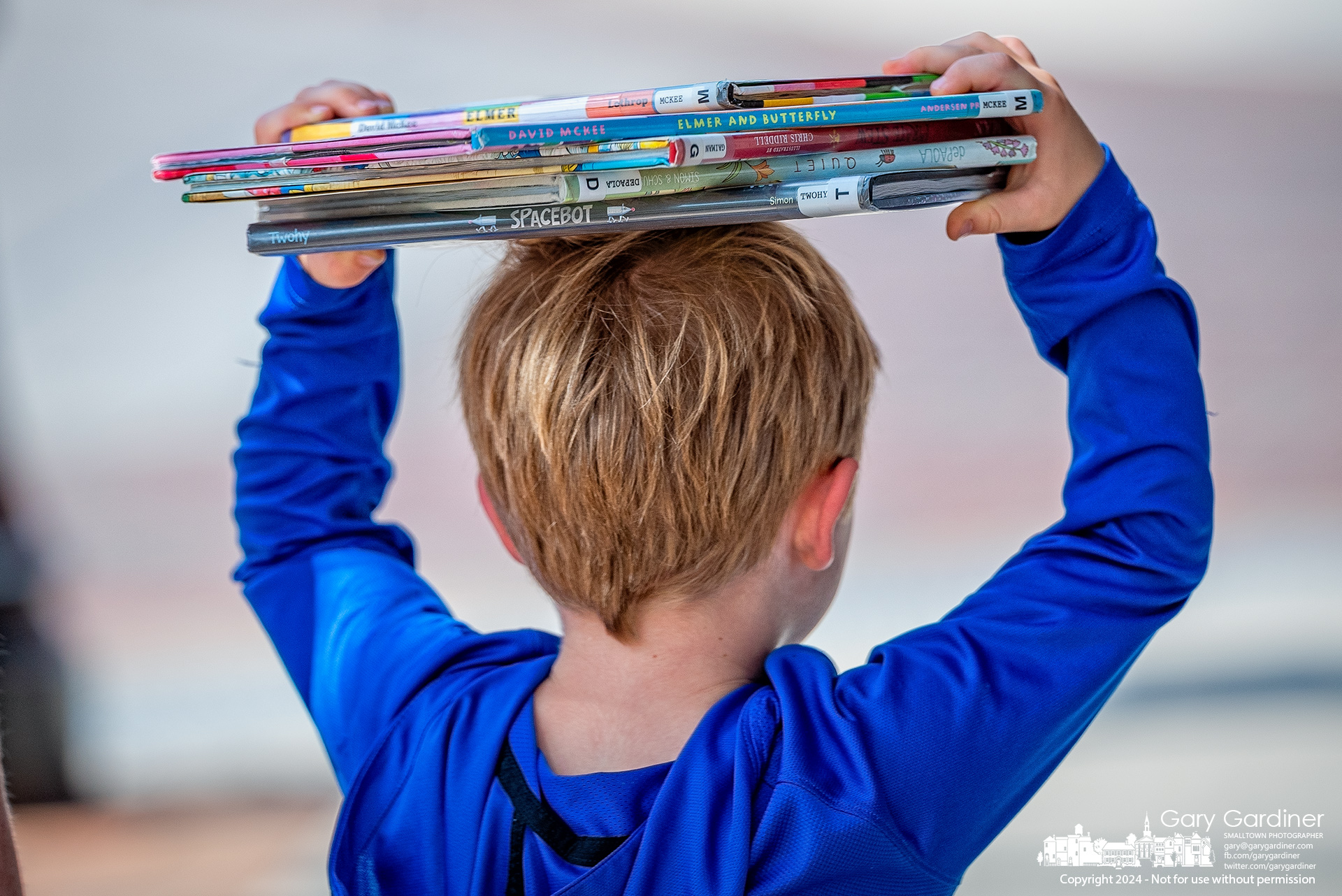 A young boy moves his library books to balance on his head after they become too heavy to carry in his arms as he walks back to the car with his family in Uptown Westerville Tuesday. My Final Photo for August 13, 2024.