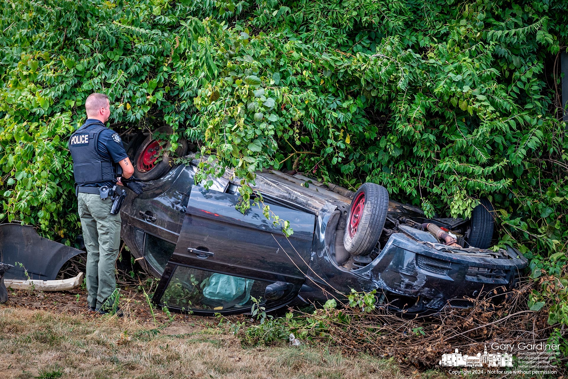 A Blendon Township police officer inspects a crashed car that landed in bushes beside Westerville Road after striking another vehicle. My Final Photo for August 30, 2024.