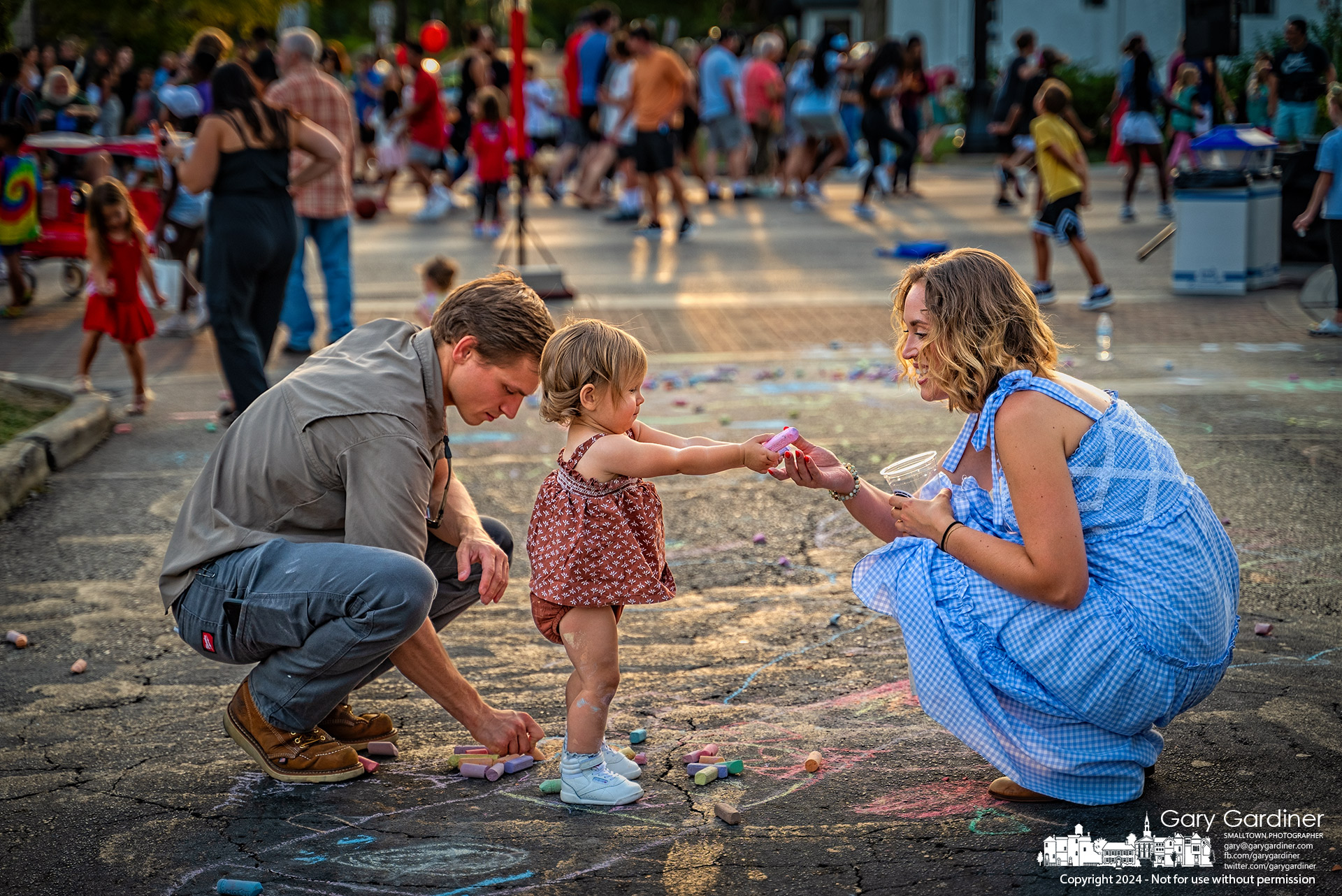 A toddler hands her mother the chalk after finishing her street art on East Park Street in an extension of Arts Alley on Fourth Friday. My Final Photo for August 23, 2024.