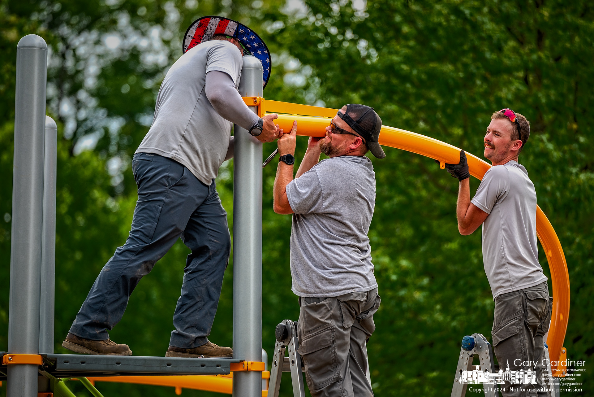 Westerville Parks workers attach an orange rib to one of the posts anchoring the new playground equipment installed at Heritage Park, replacing old equipment that had outlived its intended lifespan. My Final Photo for August 15, 2024.