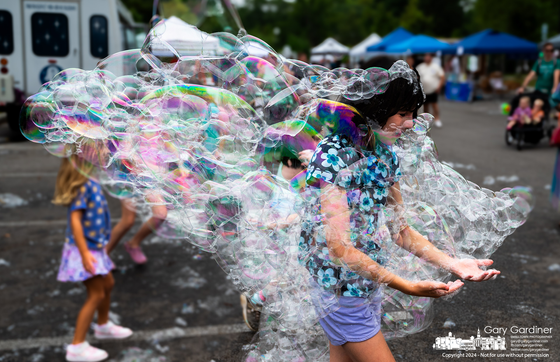 A young girl steps through a floating bundle of bubbles from the Ginat Bubble show settling into the Saturday Farmers Market in Uptown Westerville. My Final Photo for August 3, 2024.