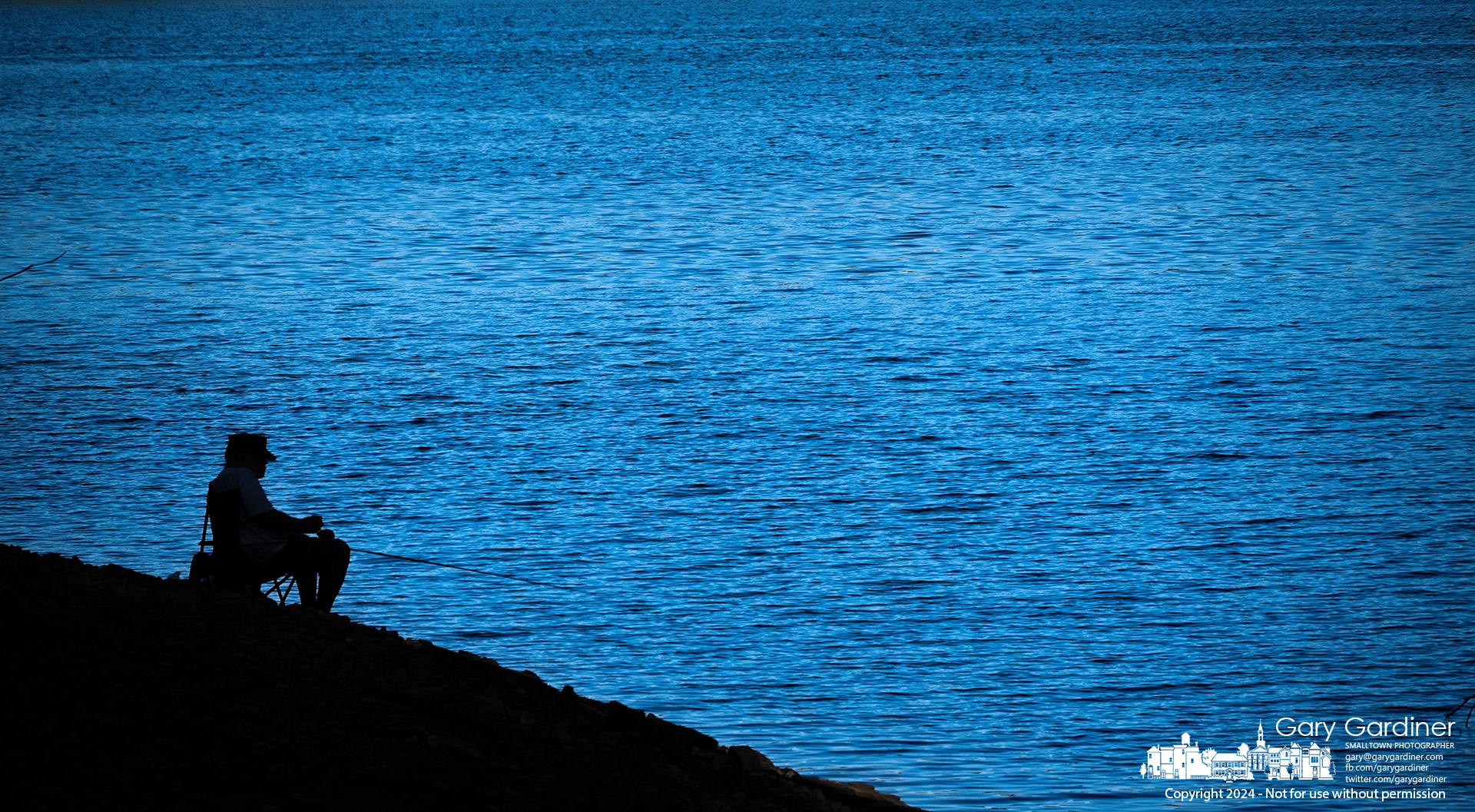 A fisherman sits in the shaded shoreline of Hoover Reservoir, silhouetted against the bright waters still lit by the late afternoon sun. My Final Photo for September 11, 2024.