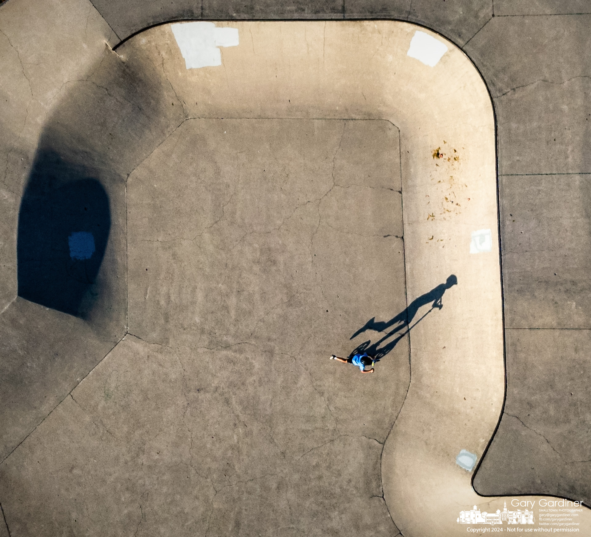 A scooter rider kicks toward the incline in a bowl at Westerville Skate Park casting his shadow across the concrete late on a warm late summer Day. My Final Photo for September 13, 2024.