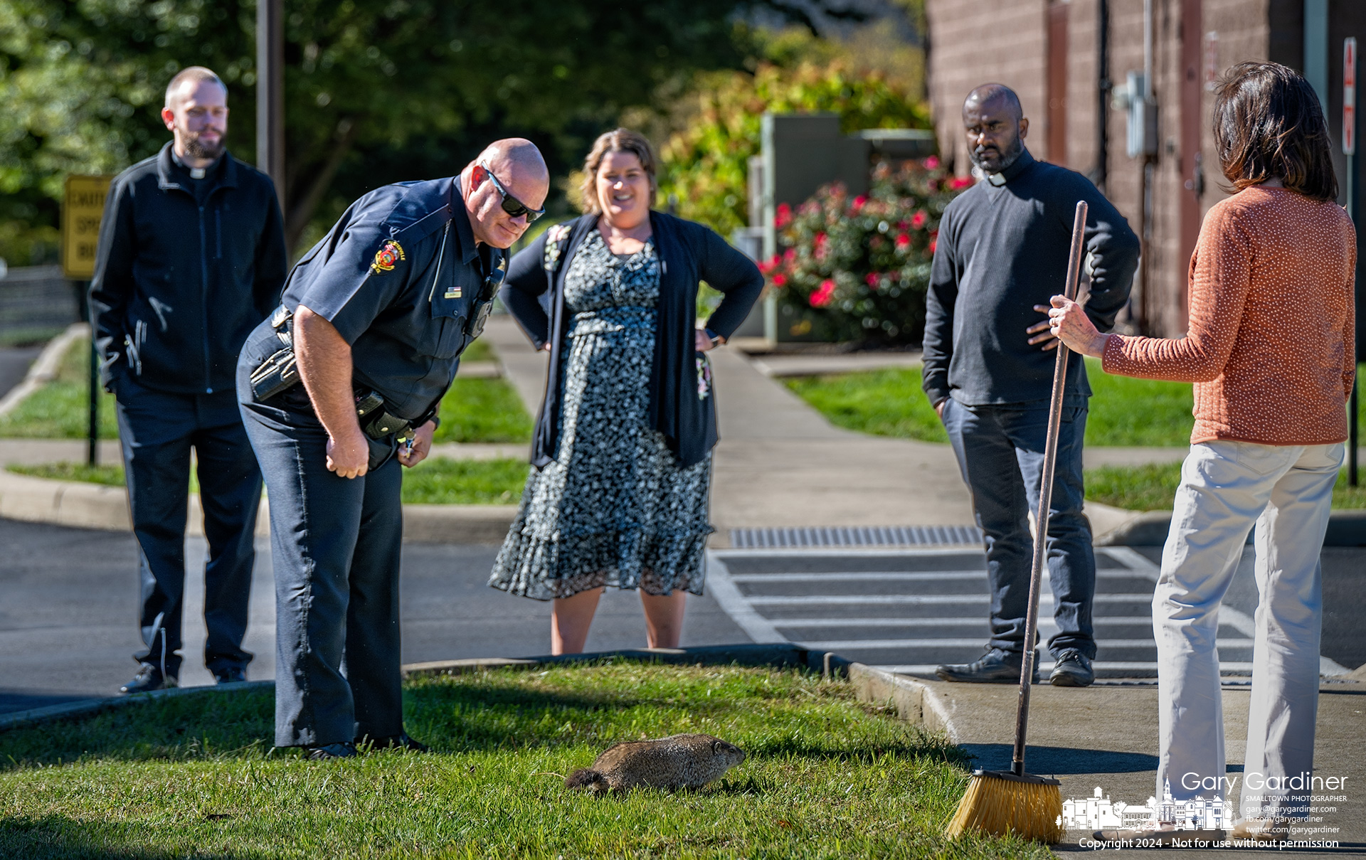 Priests and staff at St. Paul Catholic School on North State Street watch as Westerville Police Officer Jonathan Bagwell leans in to inspect a groundhog before trapping and removing the animal that appeared ill or injured outside the school Wednesday morning. My Final Photo for October 9, 2024.