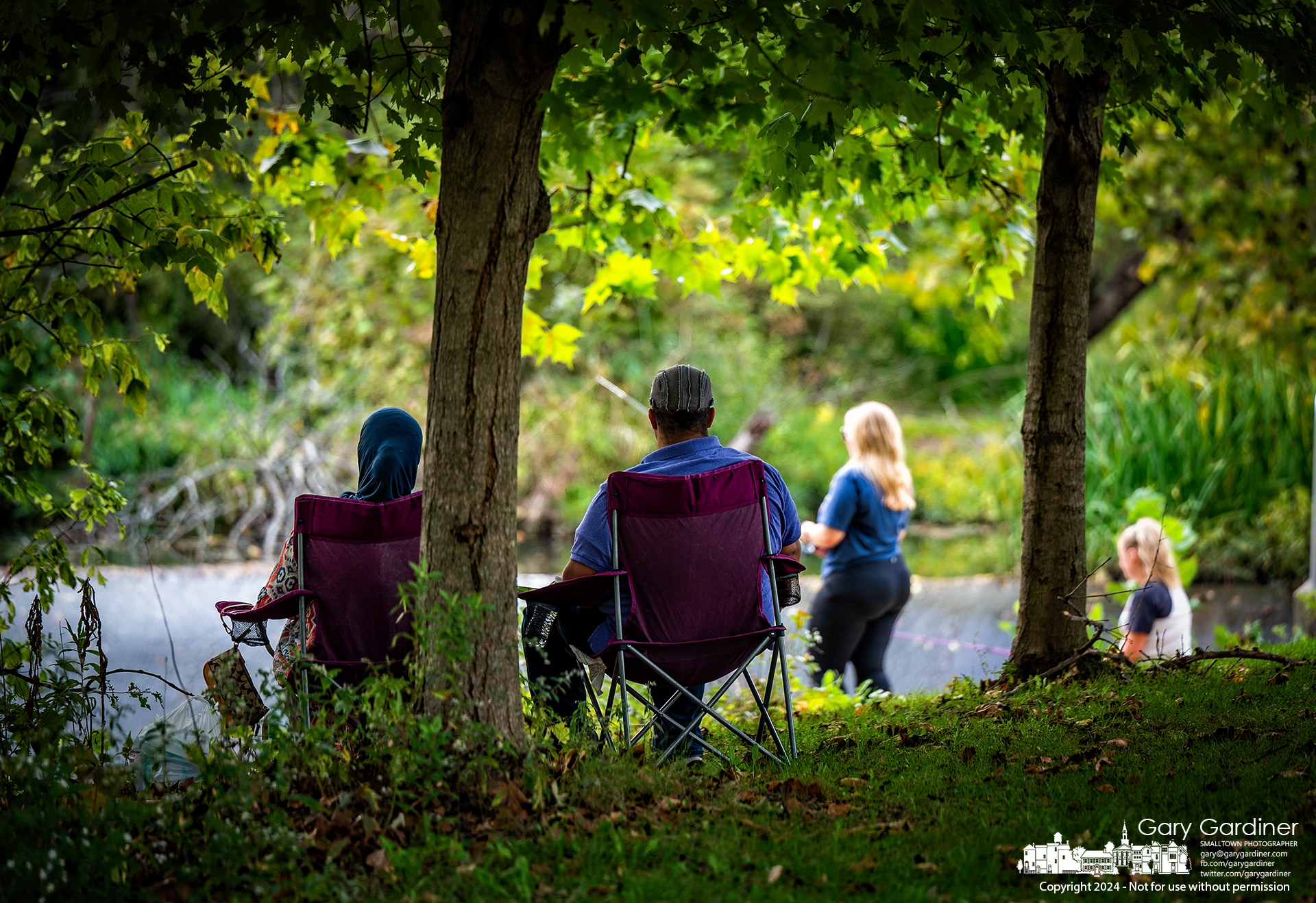 A couple sits in the shade of trees on the bank of Alum Creek, where two women hope their baits and fishing skills below the dam will be successful. My Final Photo for October 6, 2024.