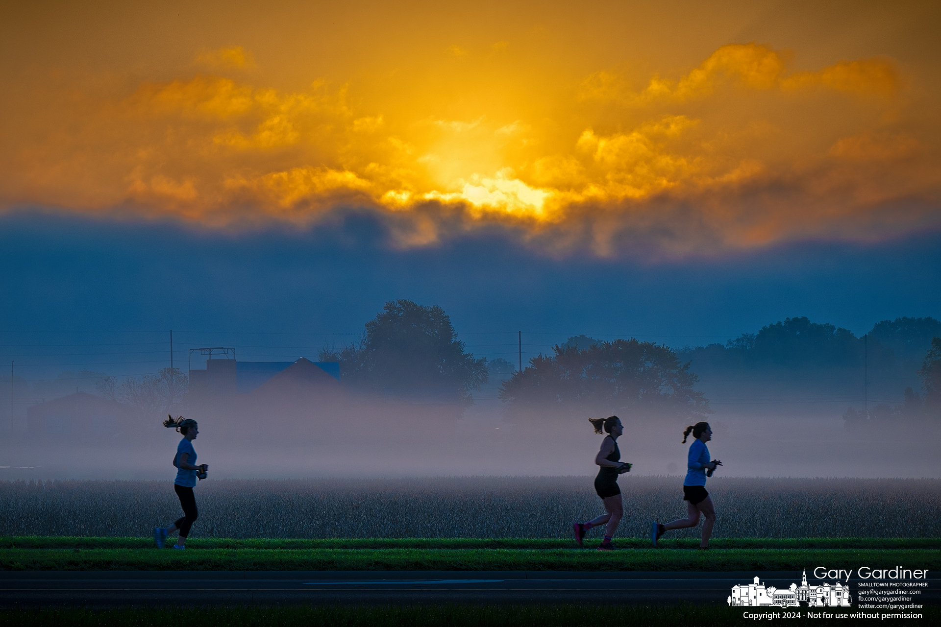 Three runners pass the fog-shrouded Yarnell Farm soybean field below the barns as the sun rises over a low-hanging layer of clouds Saturday morning. My Final Photo for October 5, 2024.