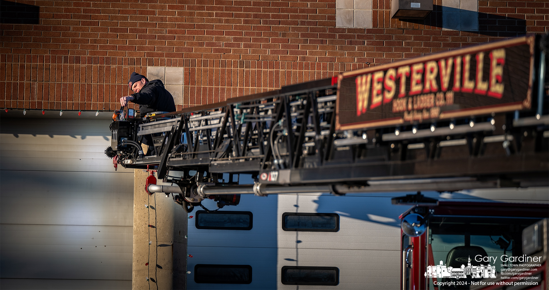 A firefighter uses the secure safety of the ladder truck to attach holiday lights to the front of Station 111 on West Main Street. My Final Photo for November 26, 2024.