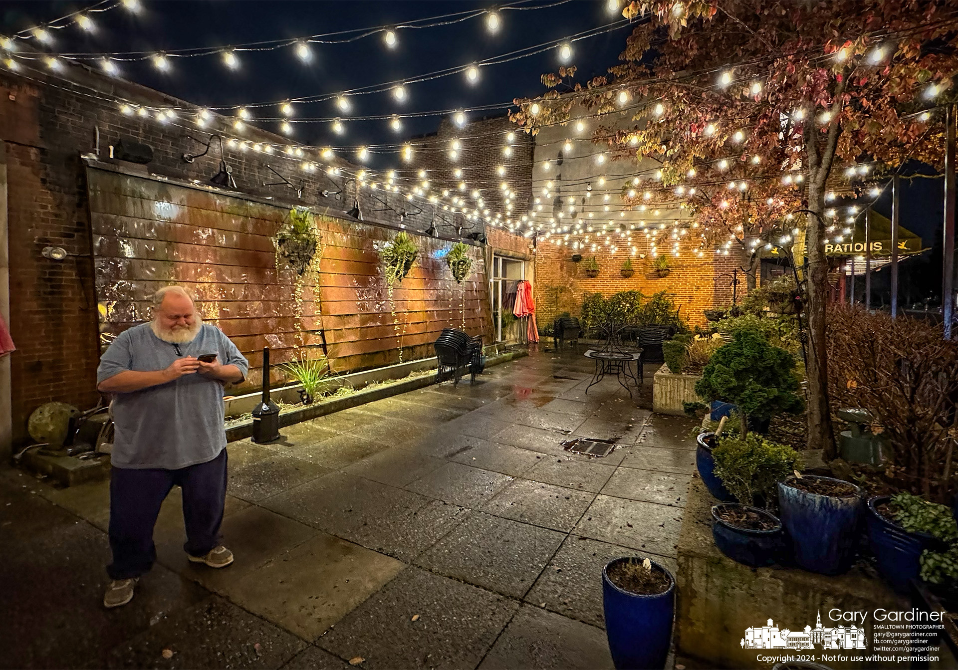 Woody Steck checks the progress of his Uber ride while standing on the now empty for winter but still illuminated patio at Jimmy V's In Uptown Westerville. My Final Photo for November 25, 2024.