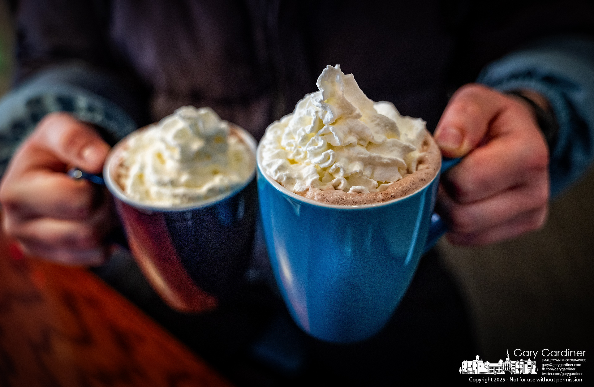 A man holds the two cups of hot chocolate swirled whipped cream he took to his table to share with a companion on a cold winter afternoon in the warmth of Java Central. My Final Photo for January 4, 2025.