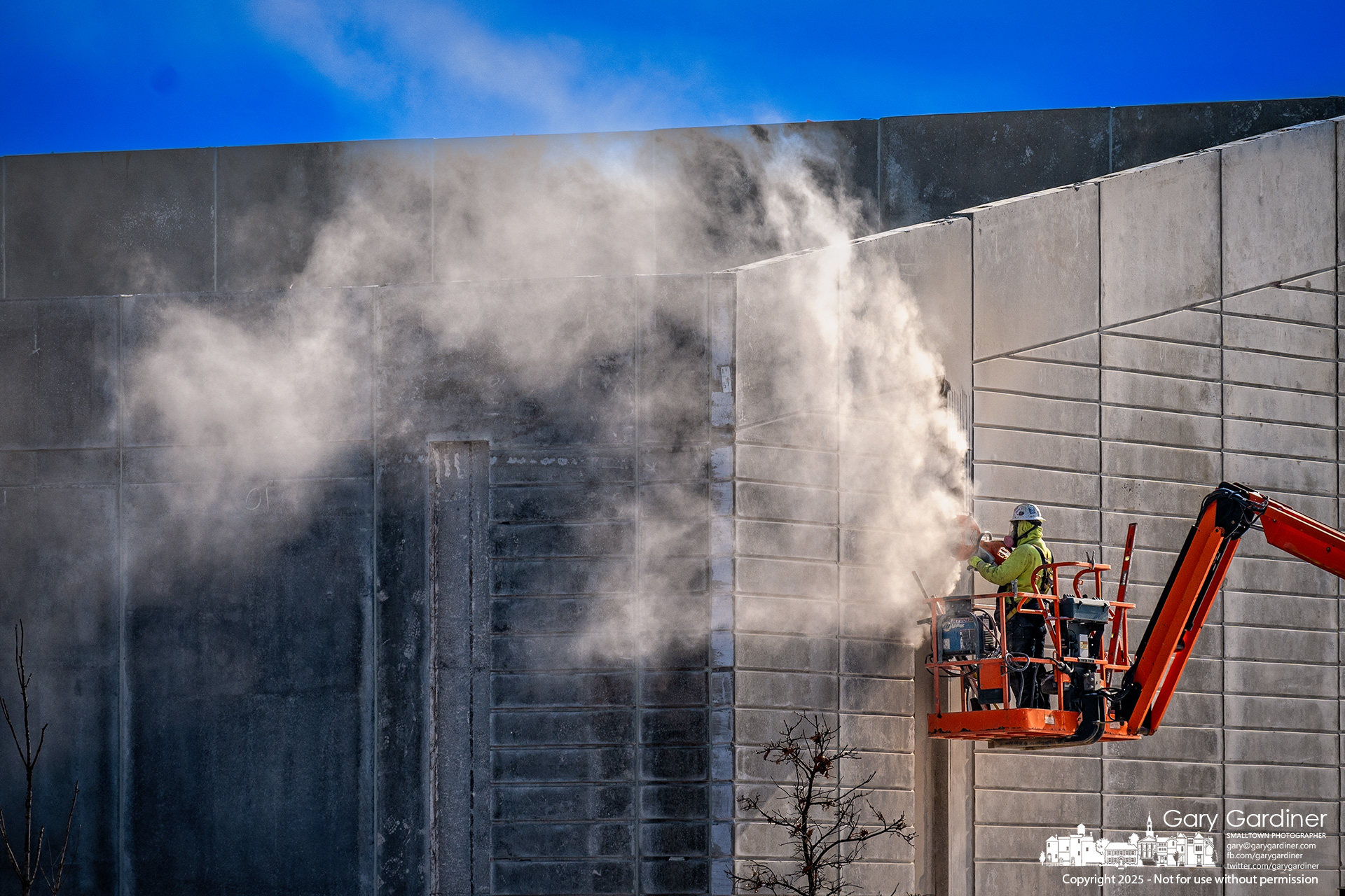 A cloud of concrete dust blows away from a worker cutting a section of one of the preformed panels installed for the outer wall of Smashpark, a sports and entertainment being built at Cleveland and Polaris. My Final Photo for January 24, 2025.