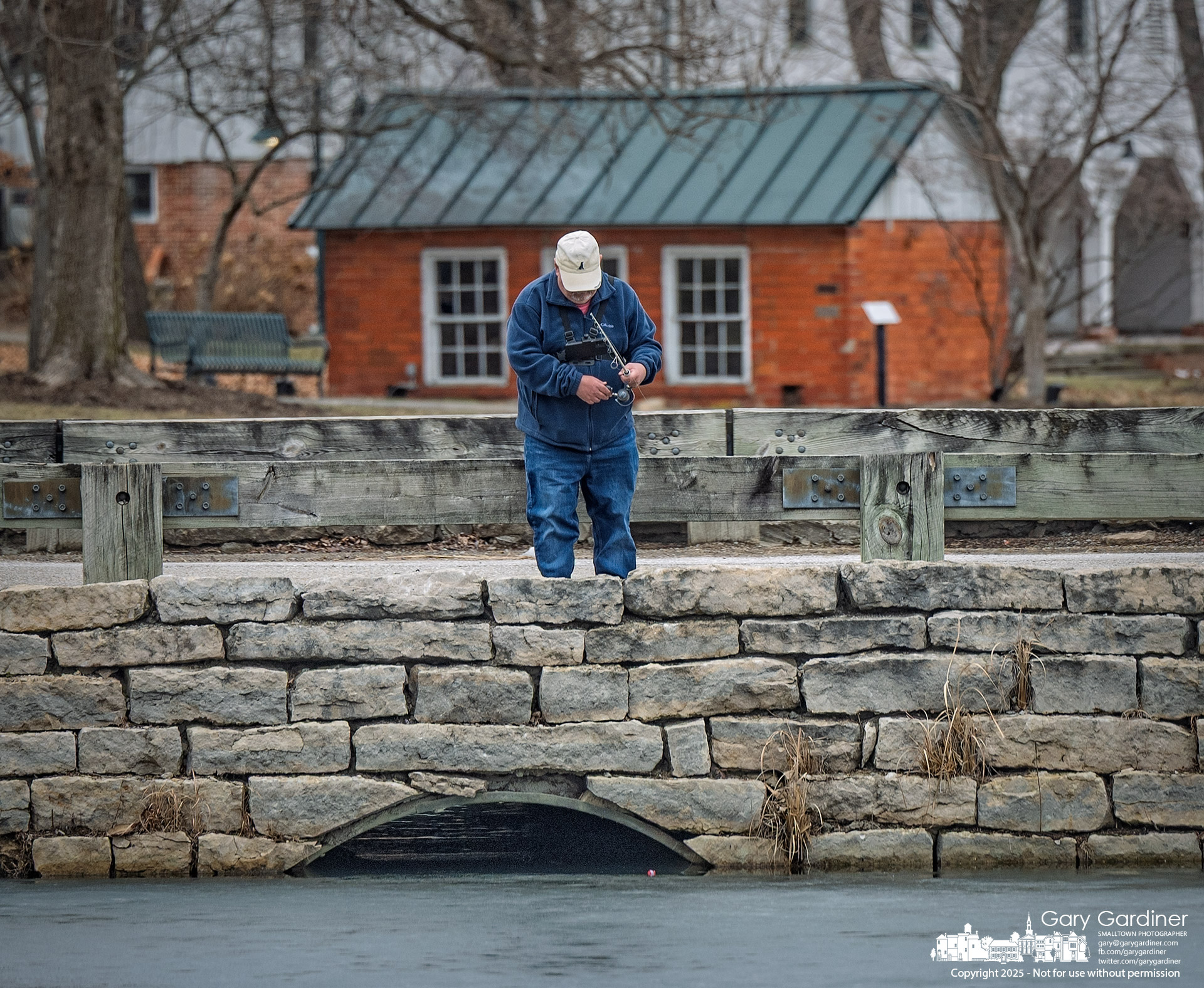 A fisherman drops his favorite lure into a hole in the partially frozen pond at Heritage Park, hoping to catch more than just a cold lure. My final Photo for February 24, 2025.