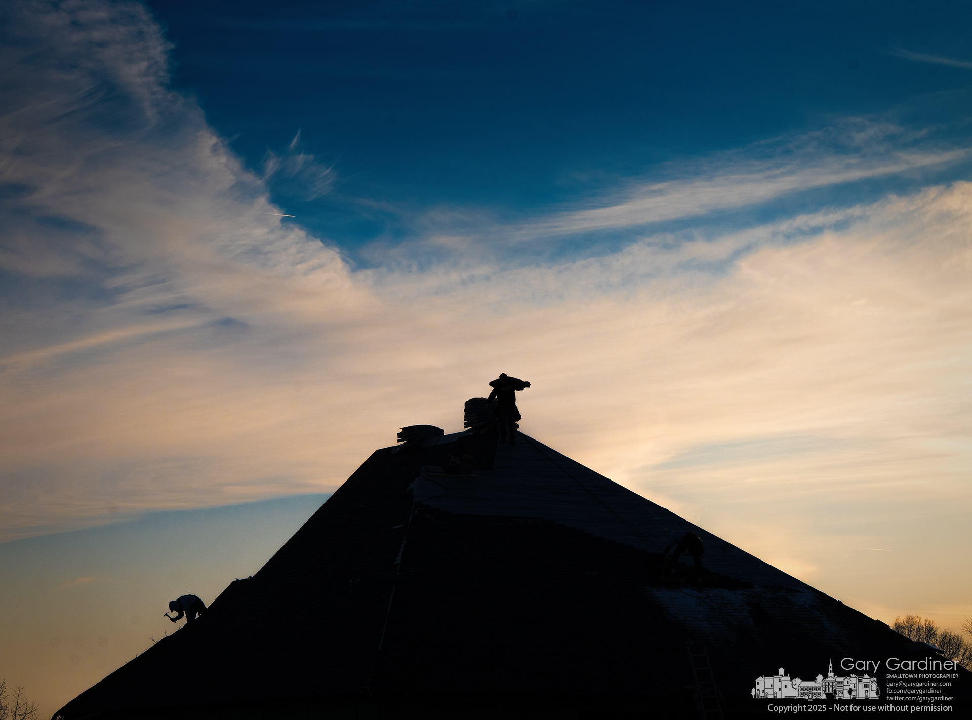 Roofers work into the winter sunset, installing shingles on a new home at Tussic and Oxbow in Genoa Township. My Final Photo for February 22, 2025.