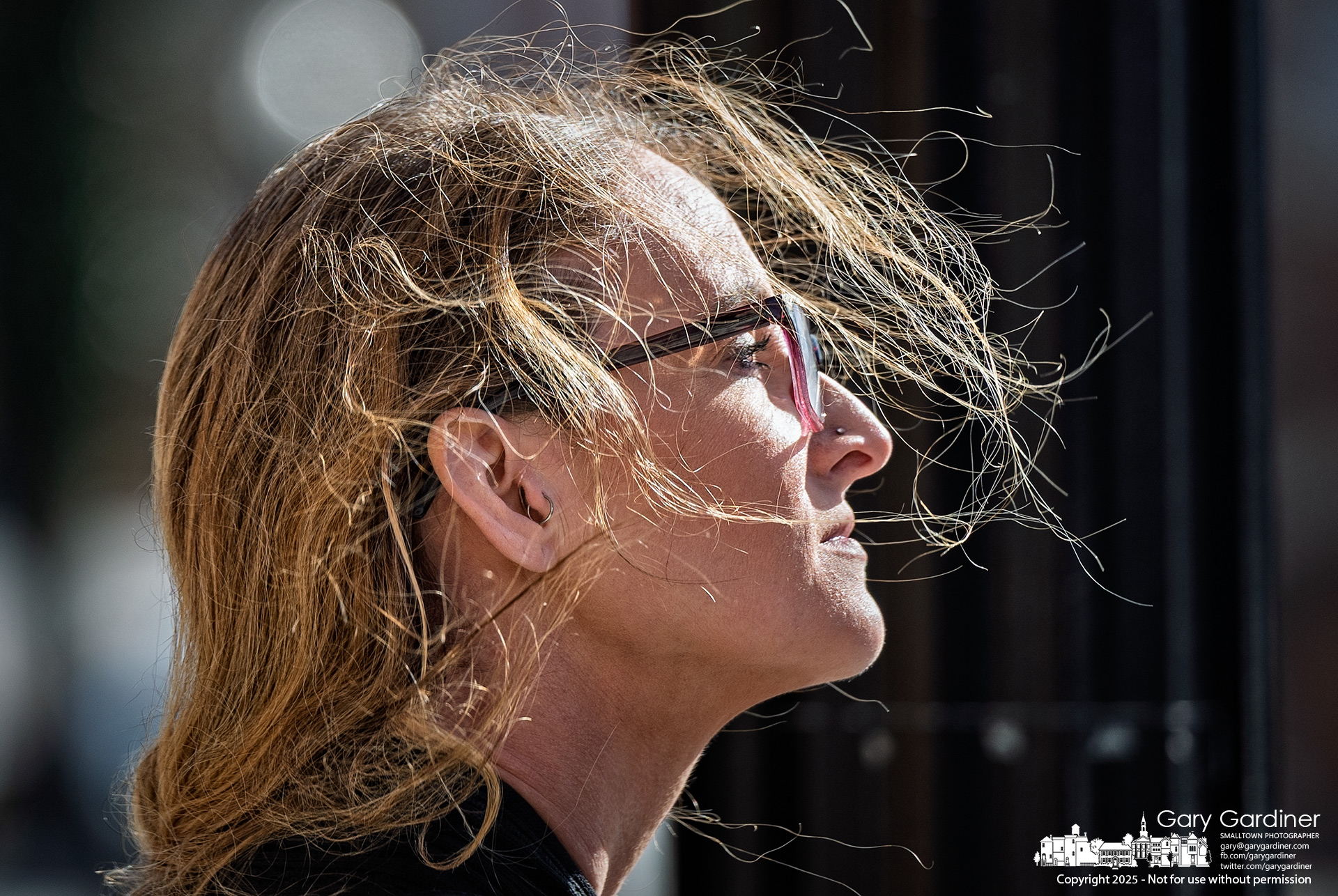 Wisps of hair fly around a woman's head as strong winds tug at her braided ponytail while she waits to cross State Street in Uptown Westerville. My Final Photo for February 28, 2025.