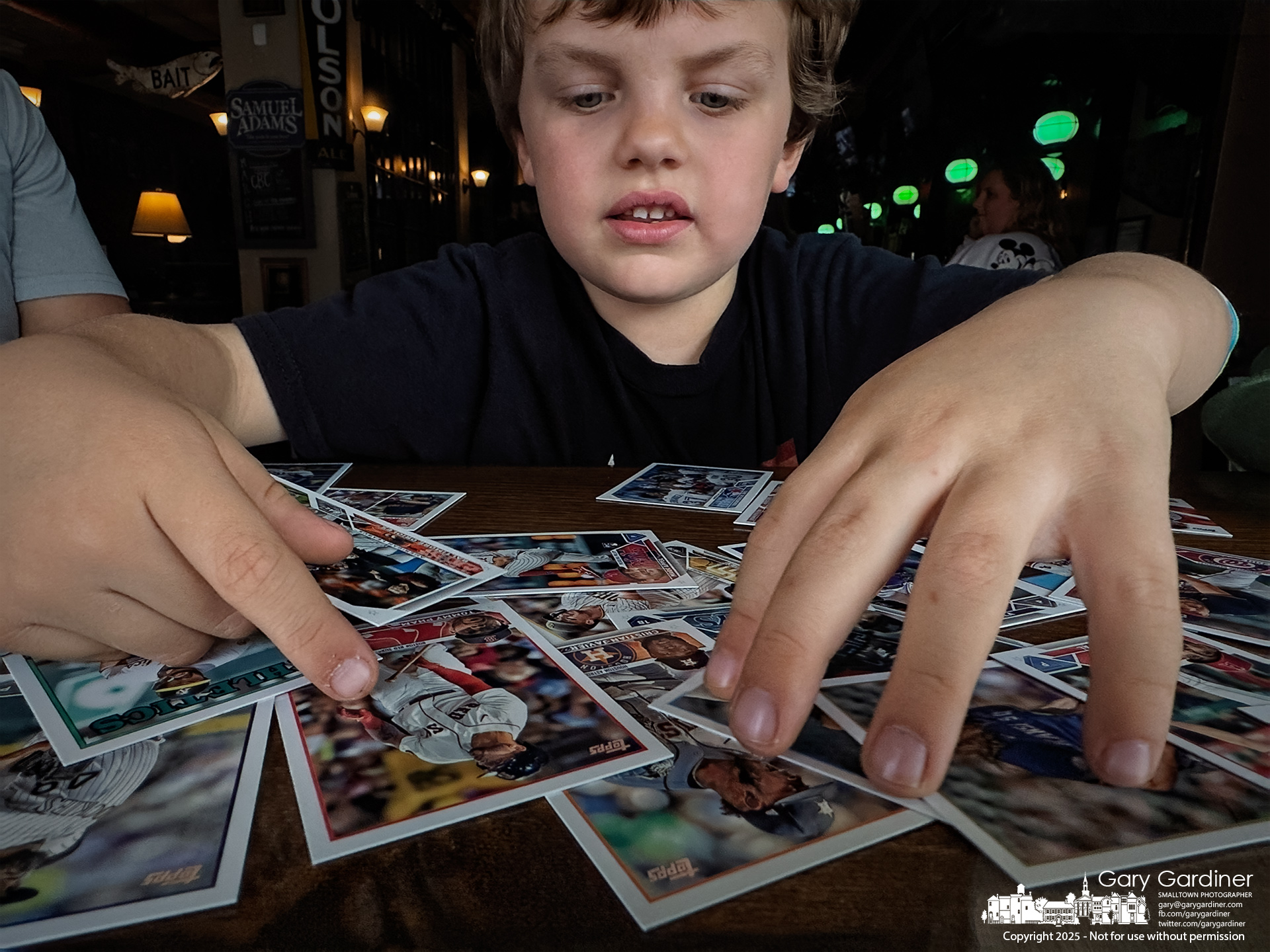 Five-year-old Sam sorts through the baseball cards his father bought for him and his two older brothers while helping them sort cards at the front window seats of Old Bag o' Nails in Uptown. My Final Photo for March 15, 2025.