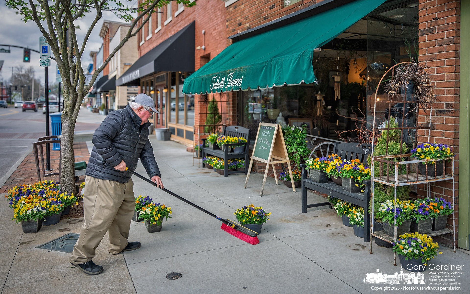 Following what he calls the “work smarter, not harder” approach, Florist Dave Talbott uses his shop broom to move his flowering pansies into a sheltered area to protect them from an overnight freeze forecast in Uptown. My Final Photo for April 7, 2025.