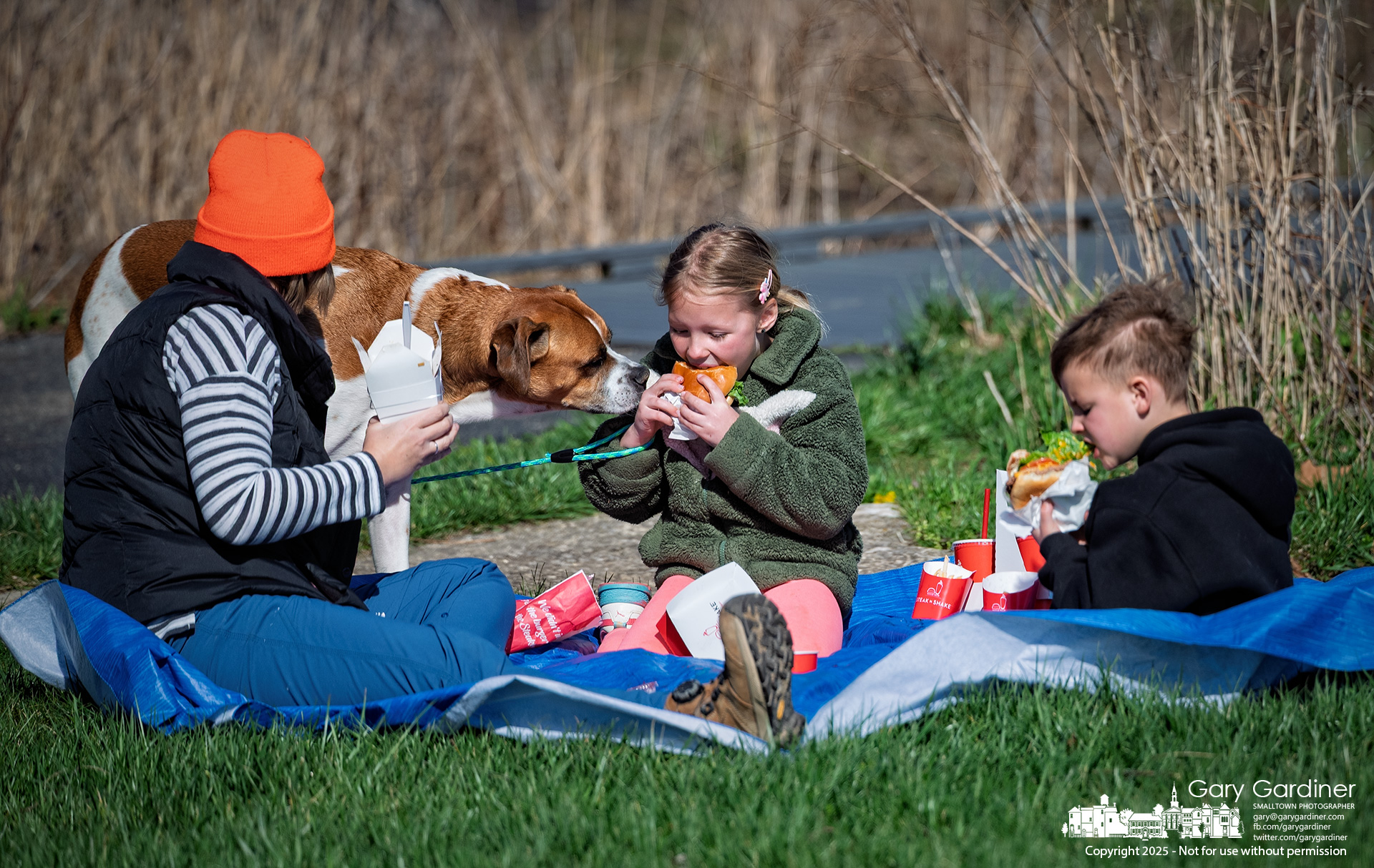 Jenny Adkins reaches to pull the family dog away from her children's burgers and fries as they enjoy a picnic in the pleasant weather at the wetlands in Highlands Park. My Final Photo for April 16, 2025.