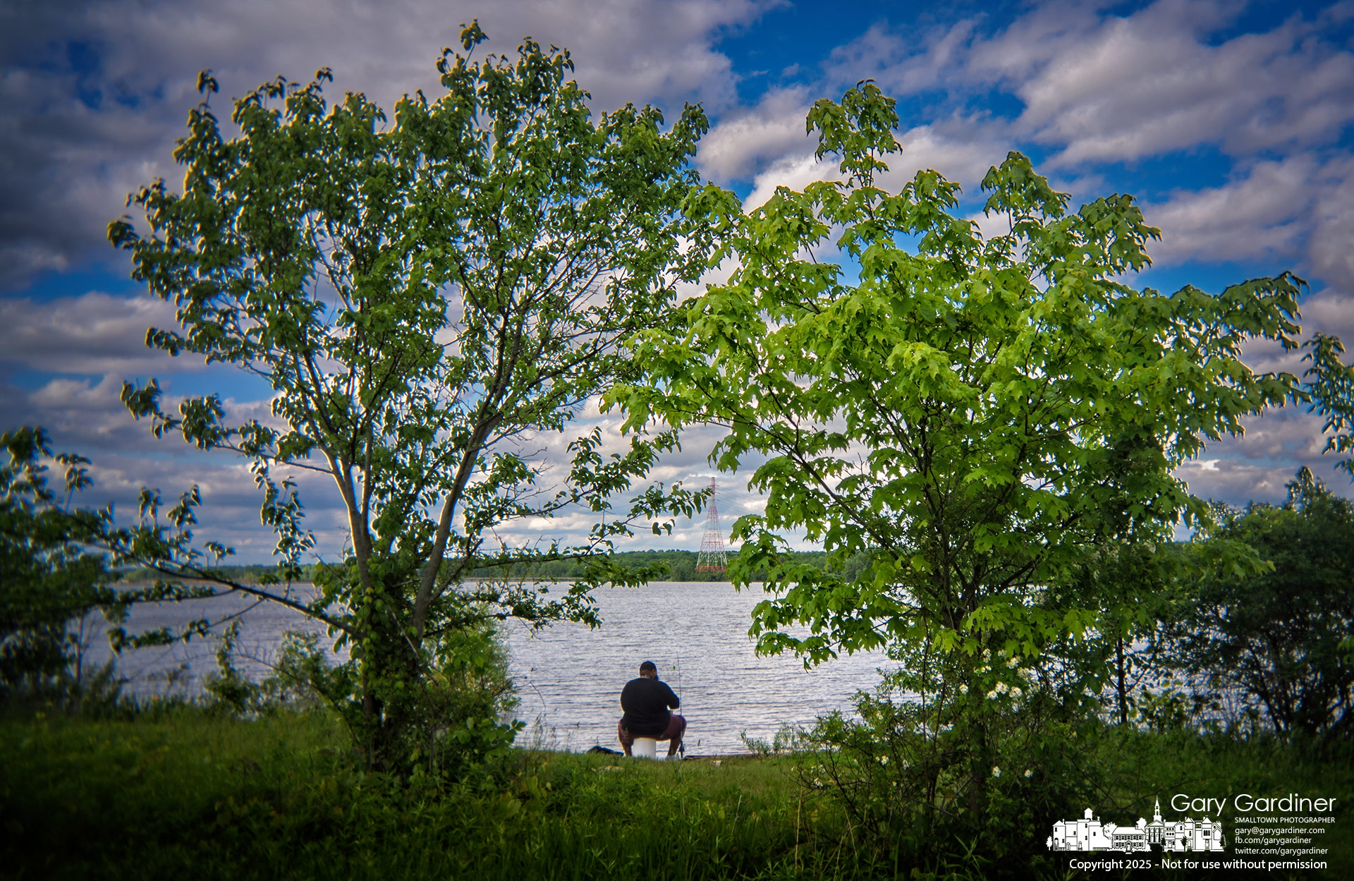 A fisherman settles into his lakeside seat, framed by two trees along the shoreline of Hoover Reservoir. My Final Photo for May 18, 2025.