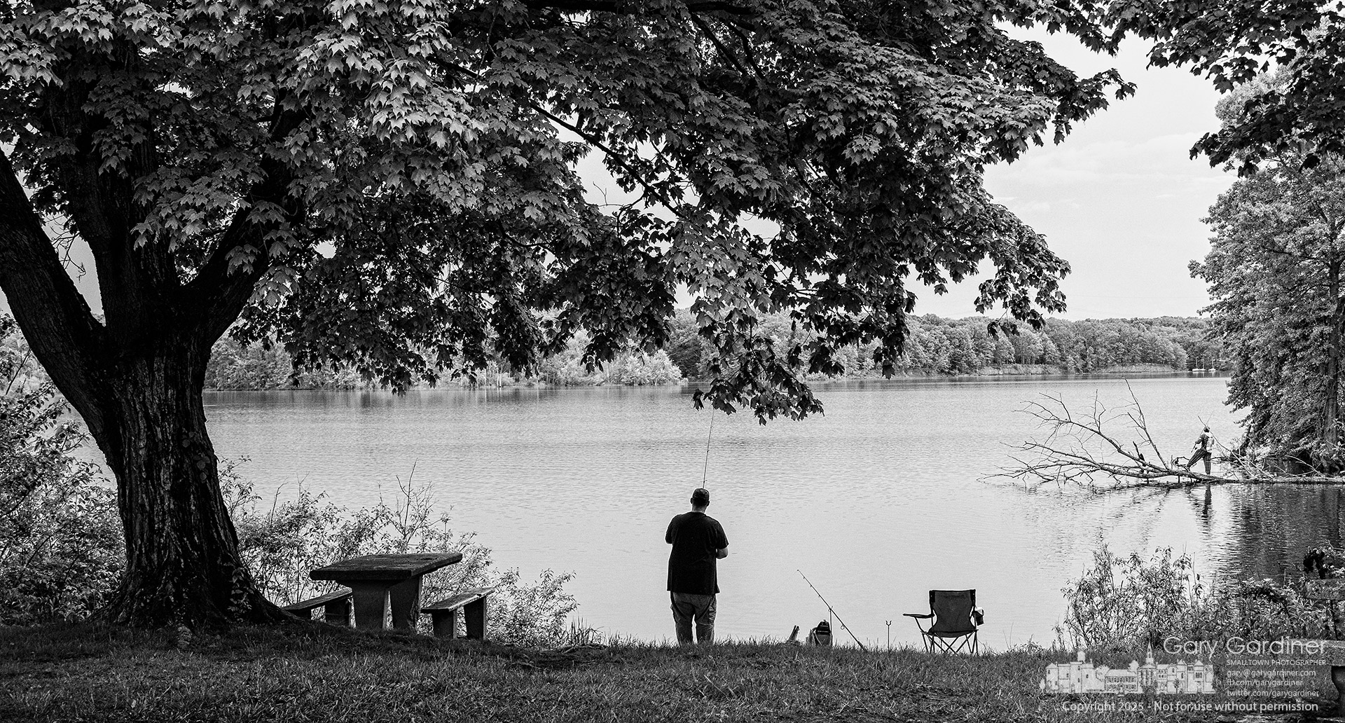 Two fishermen—one casting from the shore, the other balanced on a fallen tree—try their luck in the high waters of Hoover Reservoir at the Red Bank Boat Ramp. My Final Photo for May 13, 2025.