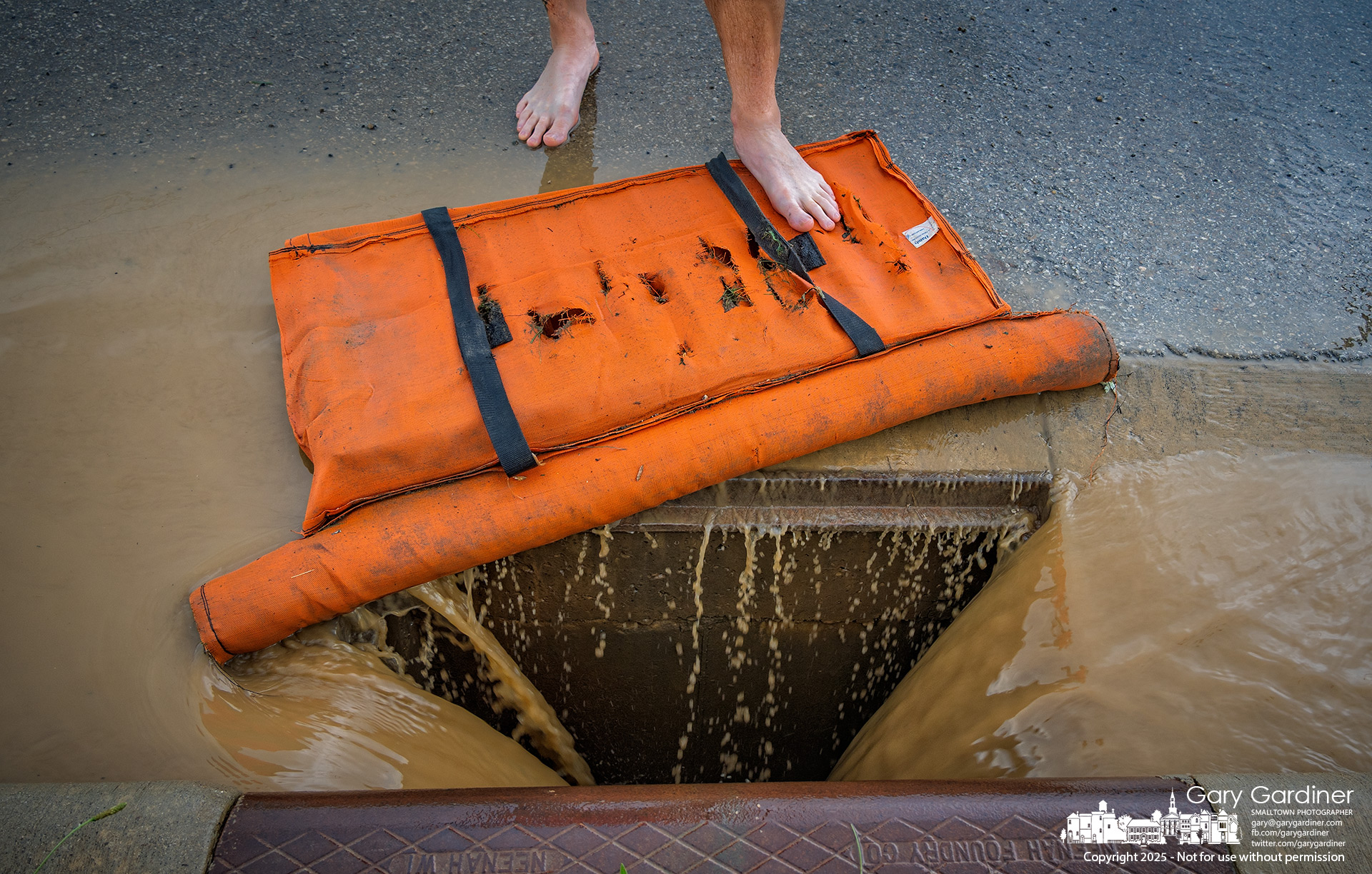 A Westerville construction inspector, oh his way to dinner with his wife, stands barefoot at a storm drain on Africa Road after temporarily removing a drainage dam that held back water flooding the road after a late afternoon storm moved across the city. My Final Photo for June 28, 2025.